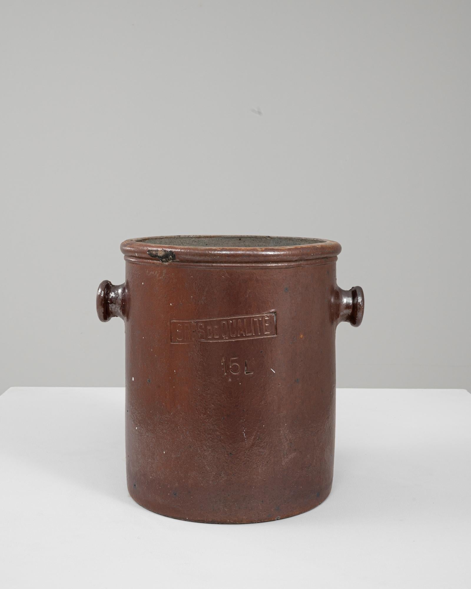 This 20th Century Belgian ceramic pot is a robust, utilitarian vessel crafted in a rich brown glaze that highlights its functional origins. Marked “Grès de Qualité” and “15 L,” it reflects the region’s long tradition of producing durable stoneware