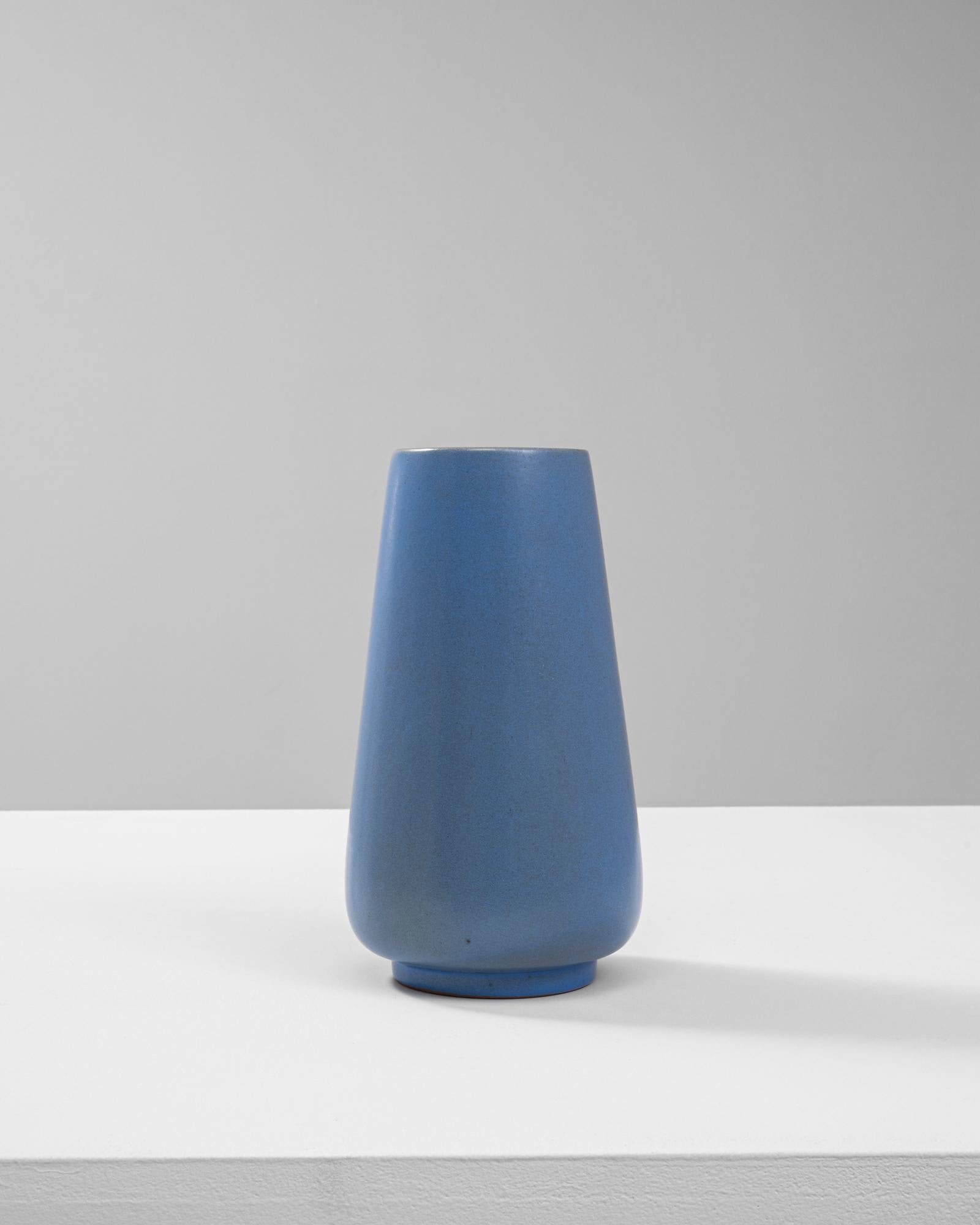 Questo vaso in ceramica belga del XX secolo presenta un design elegante e minimalista con una sorprendente finitura blu opaca. La silhouette affusolata combina linee pulite con una sottile curvatura, creando un pezzo versatile e senza tempo.