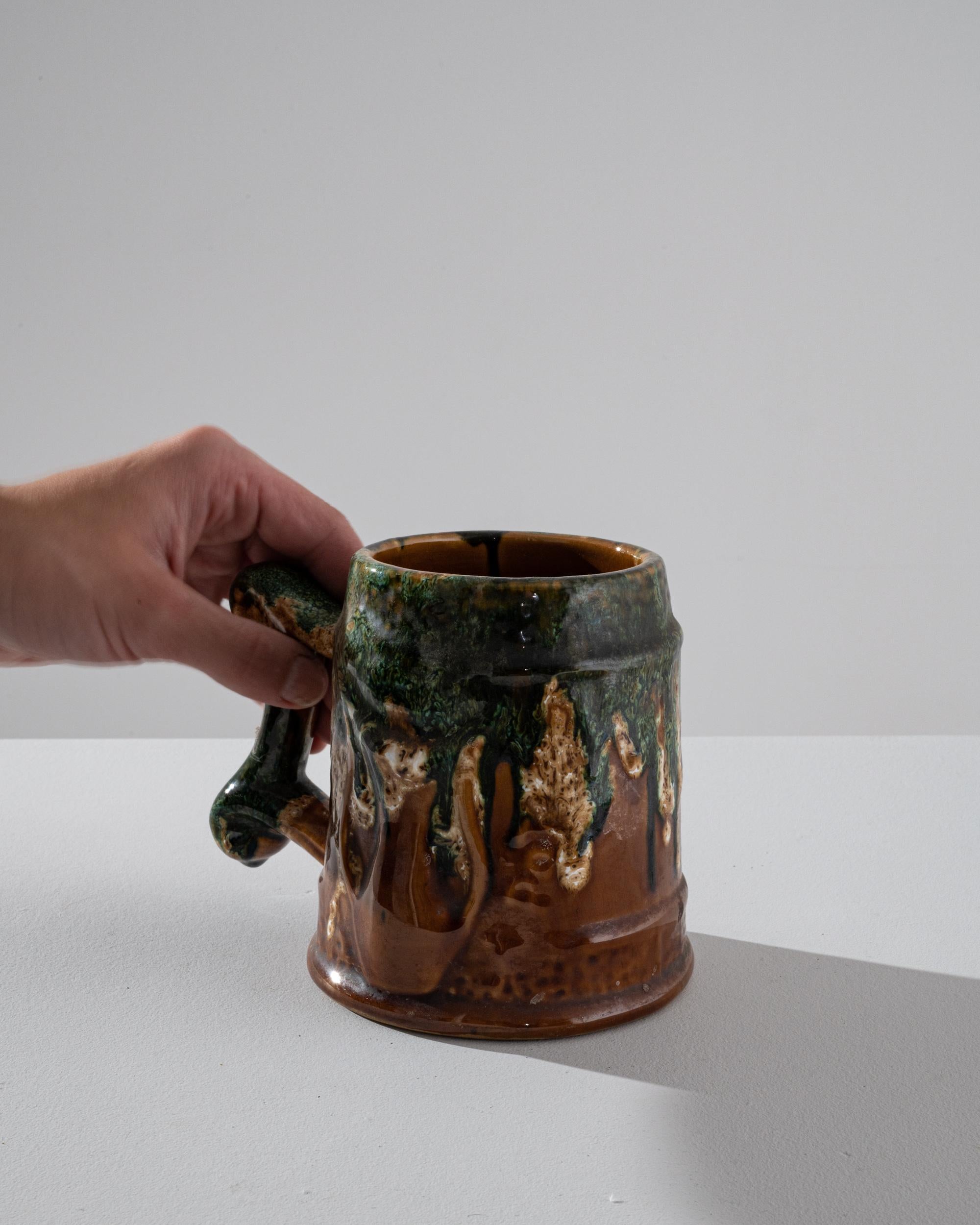 This 20th Century Belgian ceramic vase offers a unique blend of rustic charm and artistic expression. The robust form is complemented by a rich, earthy glaze that features a cascade of green over a deep brown base, reminiscent of a mossy forest
