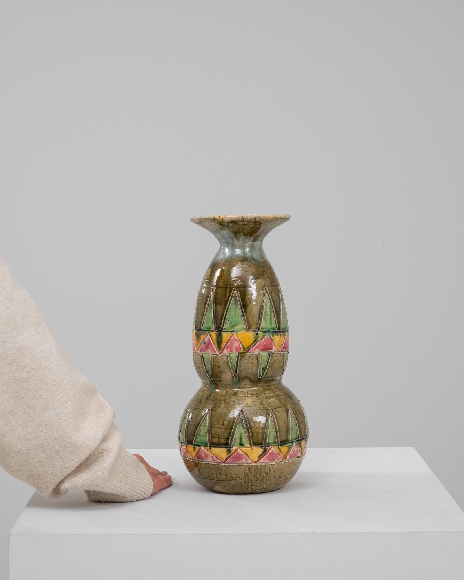 Questo esclusivo vaso in ceramica belga del XX secolo è una celebrazione di audaci motivi geometrici e toni della terra. Caratterizzato da una silhouette a doppia zucca, il vaso è ornato da intricati motivi triangolari in vivaci tonalità di verde,