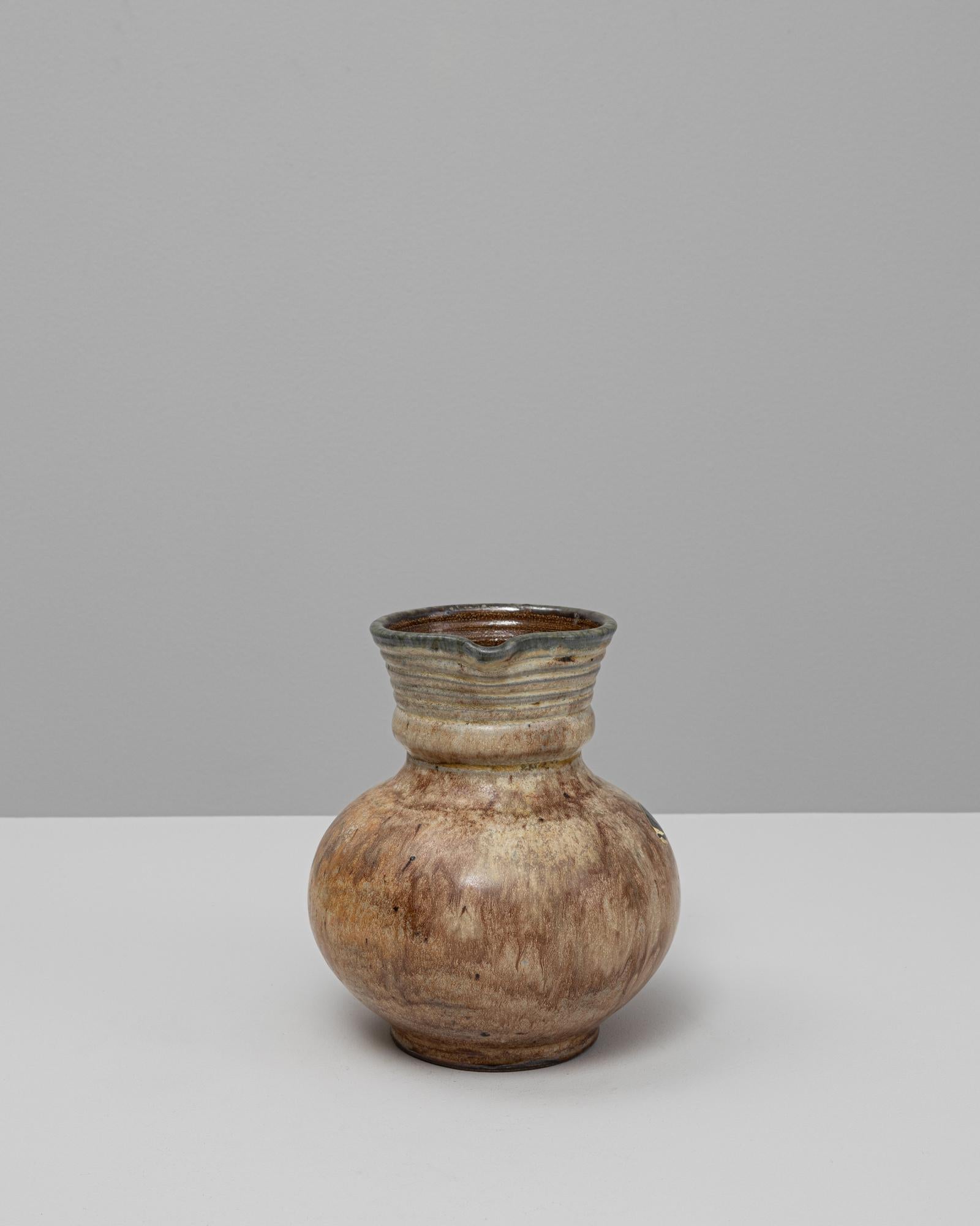 Ce vase en céramique belge du 20e siècle présente une esthétique chaleureuse et organique définie par sa silhouette arrondie et sa glaçure doucement texturée. Le corps bulbeux se transforme en un col nervuré, semblable à une collerette, avec un bec