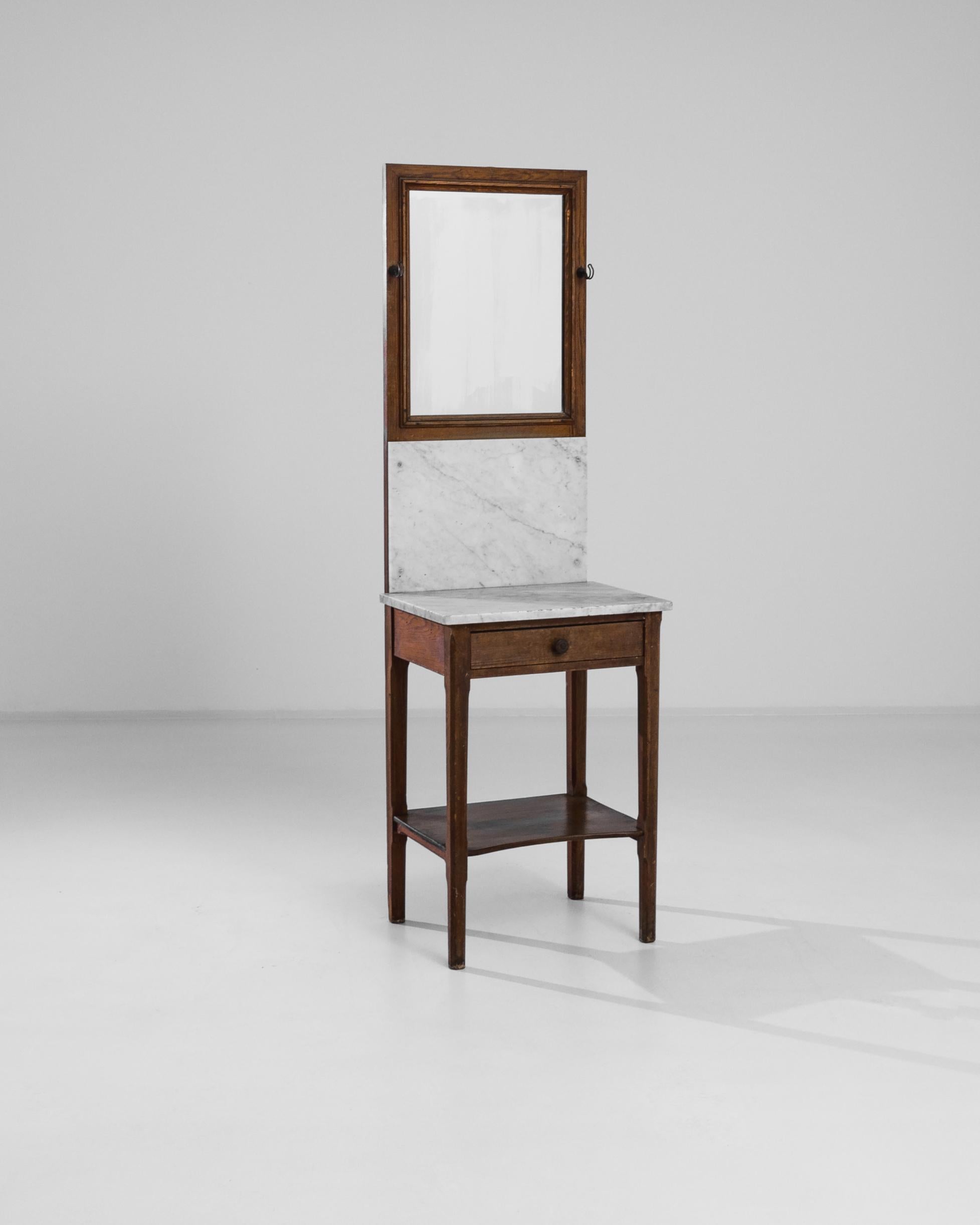 This curious tall dressing table was handcrafted in Belgium circa 1910. The combination of the dark wooden base with the white marble top imparts a luxurious feel punctuated by the silhouette of the slender legs. The mirror with two practical hooks