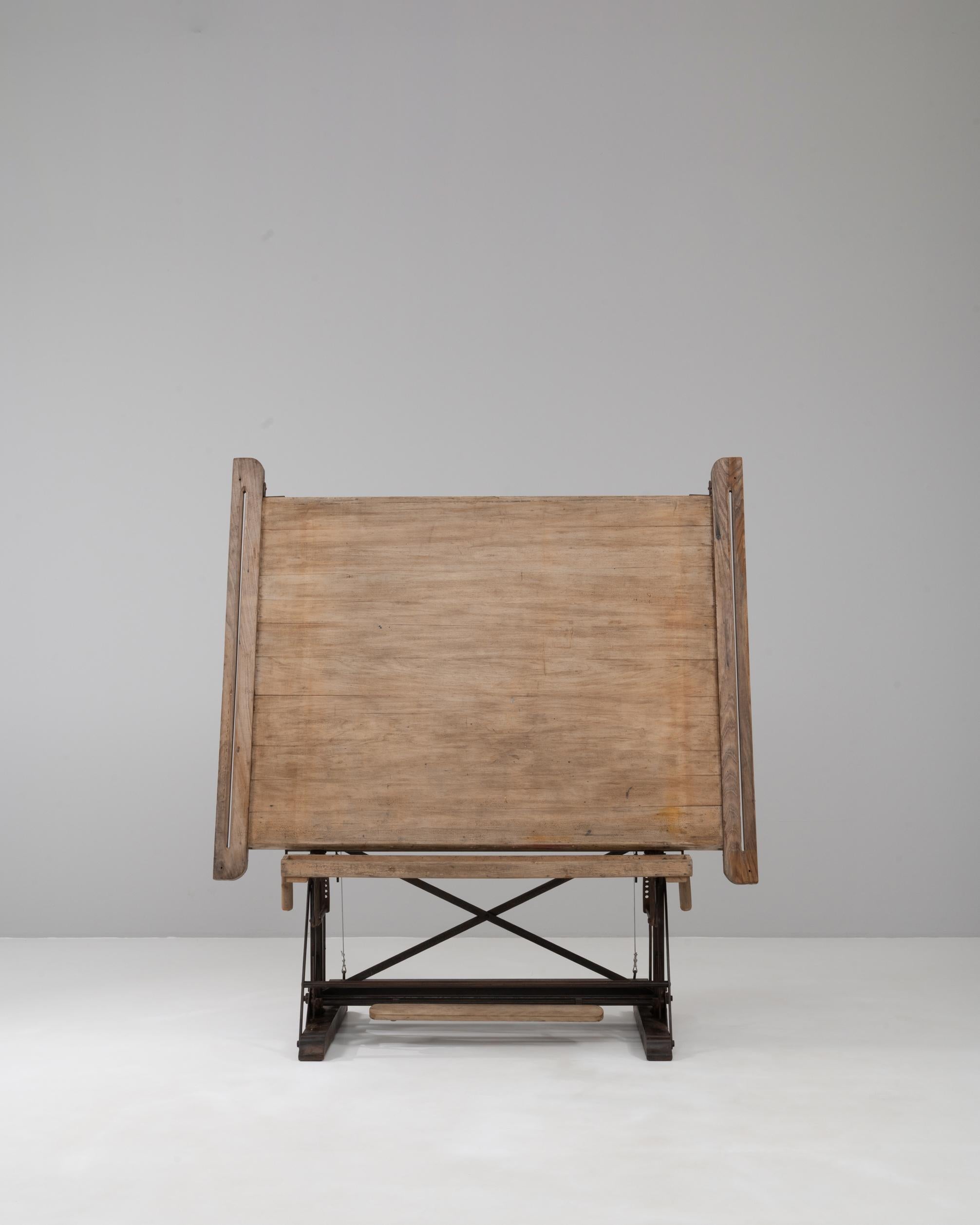 Table à dessin industrielle belge du 20e siècle, avec un plateau en bois massif soutenu par une base en fer réglable. La surface peut être inclinée selon différents angles, ce qui est idéal pour la rédaction ou l'affichage, tandis que la pédale