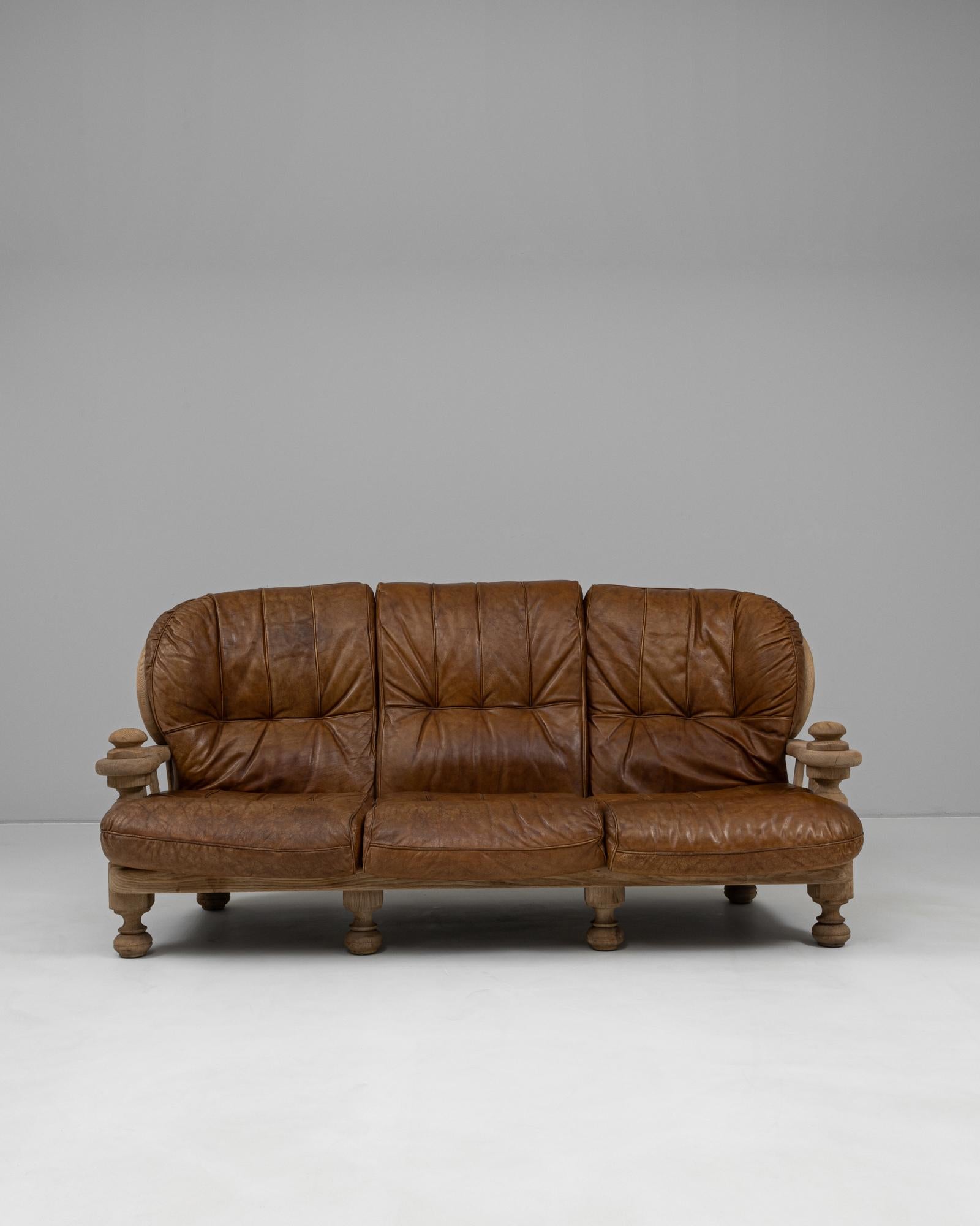 Ce canapé en cuir belge du XXe siècle allie un travail du bois sculptural à un confort profond et accueillant, ce qui en fait une pièce d'apparat frappante à la présence indéniable. Le cadre en bois massif, laissé dans une finition naturelle