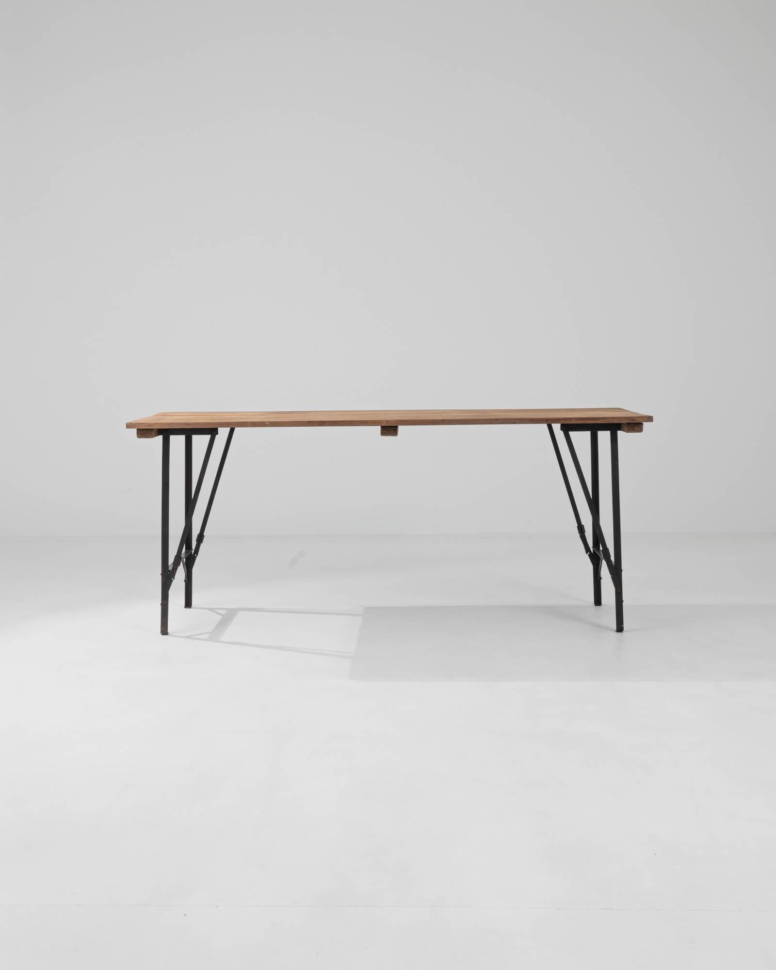 Simple yet marvelously versatile, this rustic table offers an attractive vintage accent. Built in Belgium in the 20th century, the lightweight form is composed of a tabletop of natural wooden boards set atop a slender metal frame. Hinged legs, held