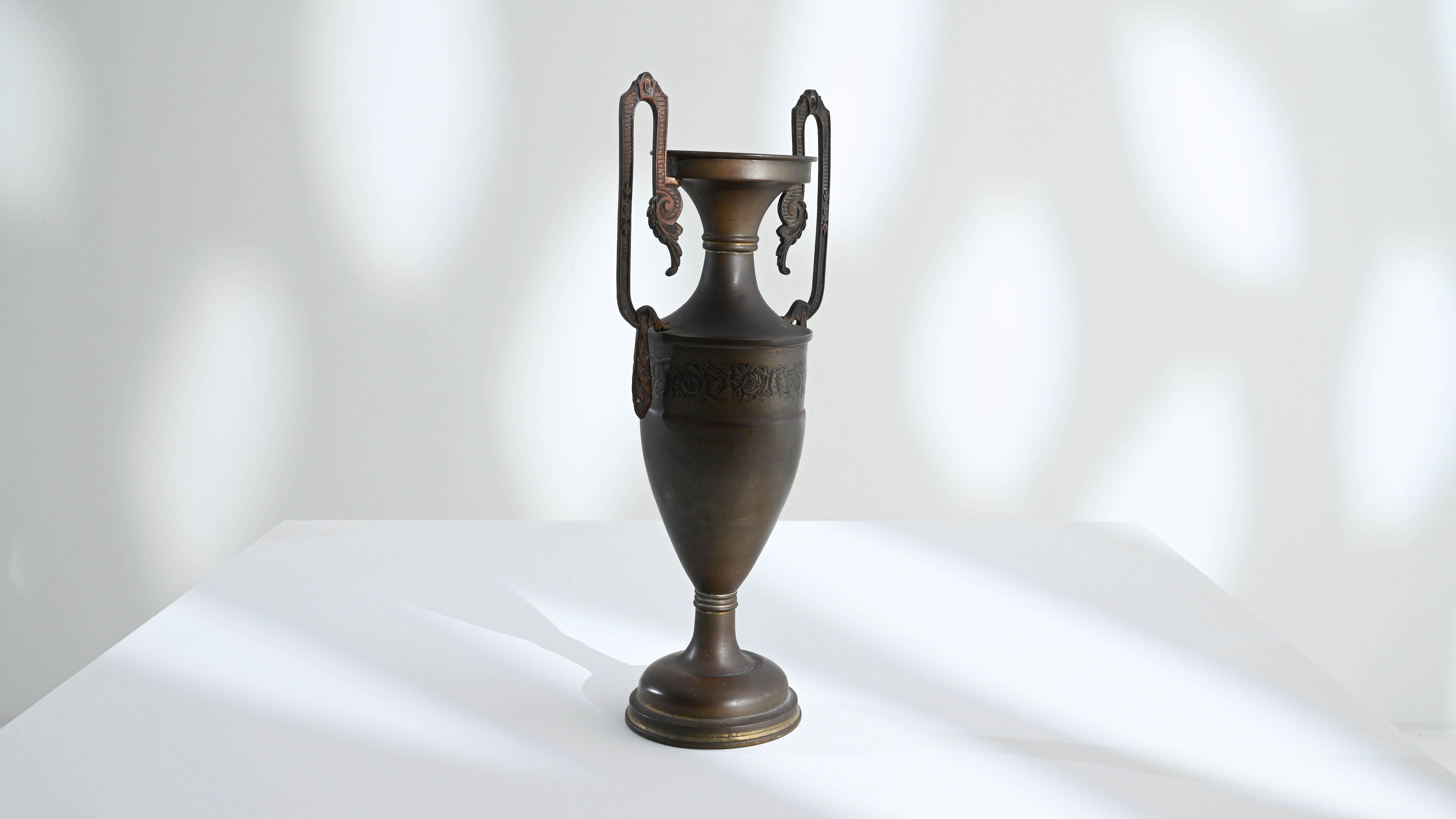 A metal vase created in 20th century France. With elaborate handles, a delicately tapered vessel body, and no shortage of lovingly crafted details, this vase stuns the eye with its attention to detail and hand-made craftsmanship. Painstakingly
