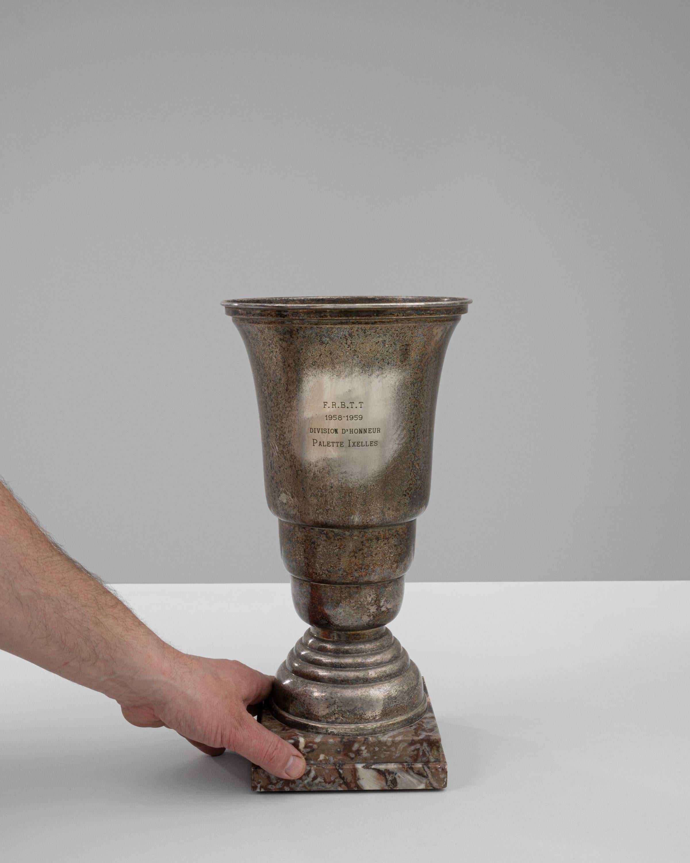 Diese belgische Pokaltrophäe aus dem 20. Jahrhundert, die vom Geist des Wettbewerbs durchdrungen ist, ist ein großartiger Fund für Sammler und Sportbegeisterte gleichermaßen. Die Trophäe, die aus einer Mischung aus haltbarem Metall und reichem