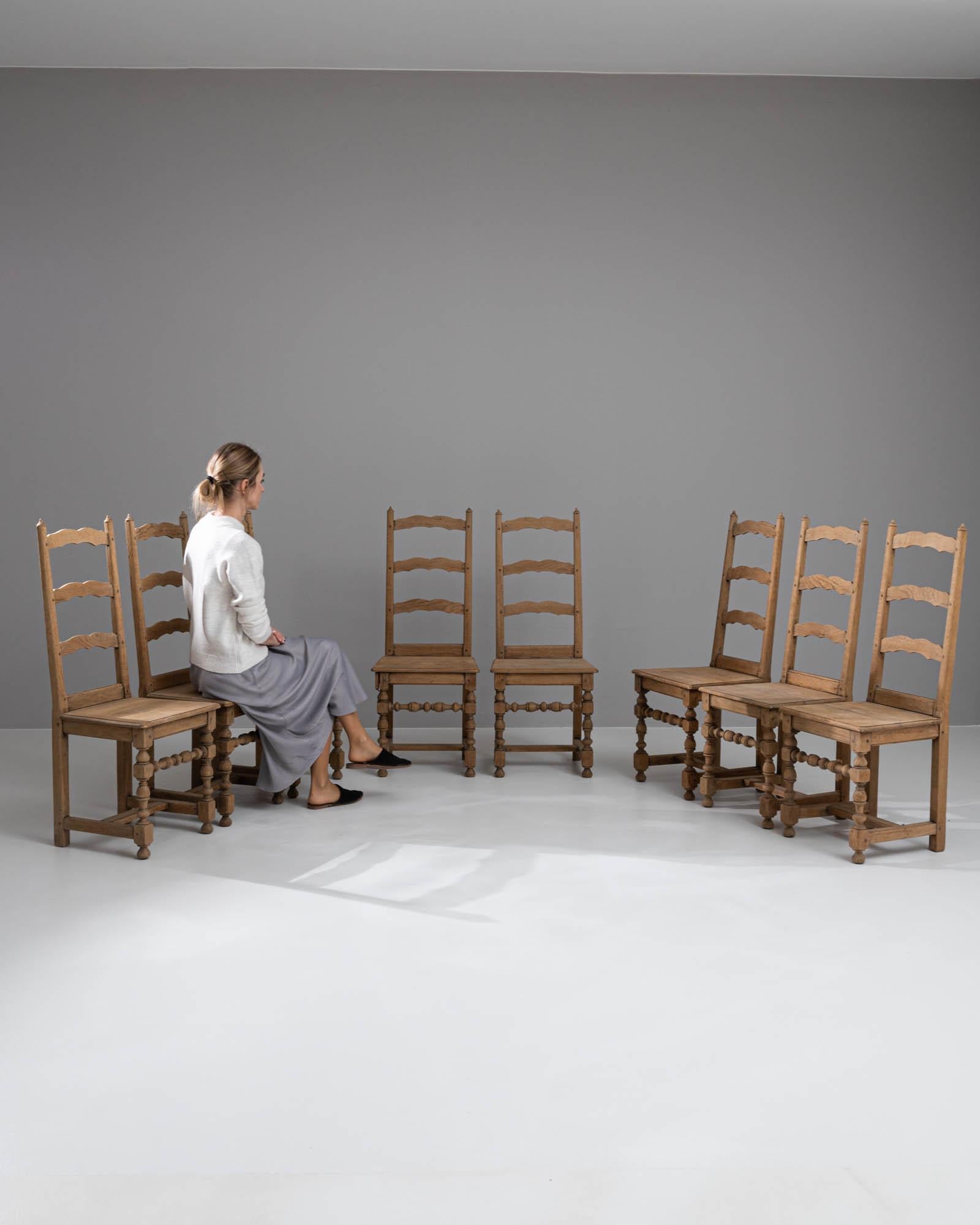 Wir stellen Ihnen ein Set von acht belgischen Eichenstühlen aus dem 20. Jahrhundert vor, die von robuster Eleganz und rustikalem Charme zeugen. Jeder Stuhl hat eine beeindruckende Präsenz und die natürliche Maserung der Eiche erzählt Geschichten aus