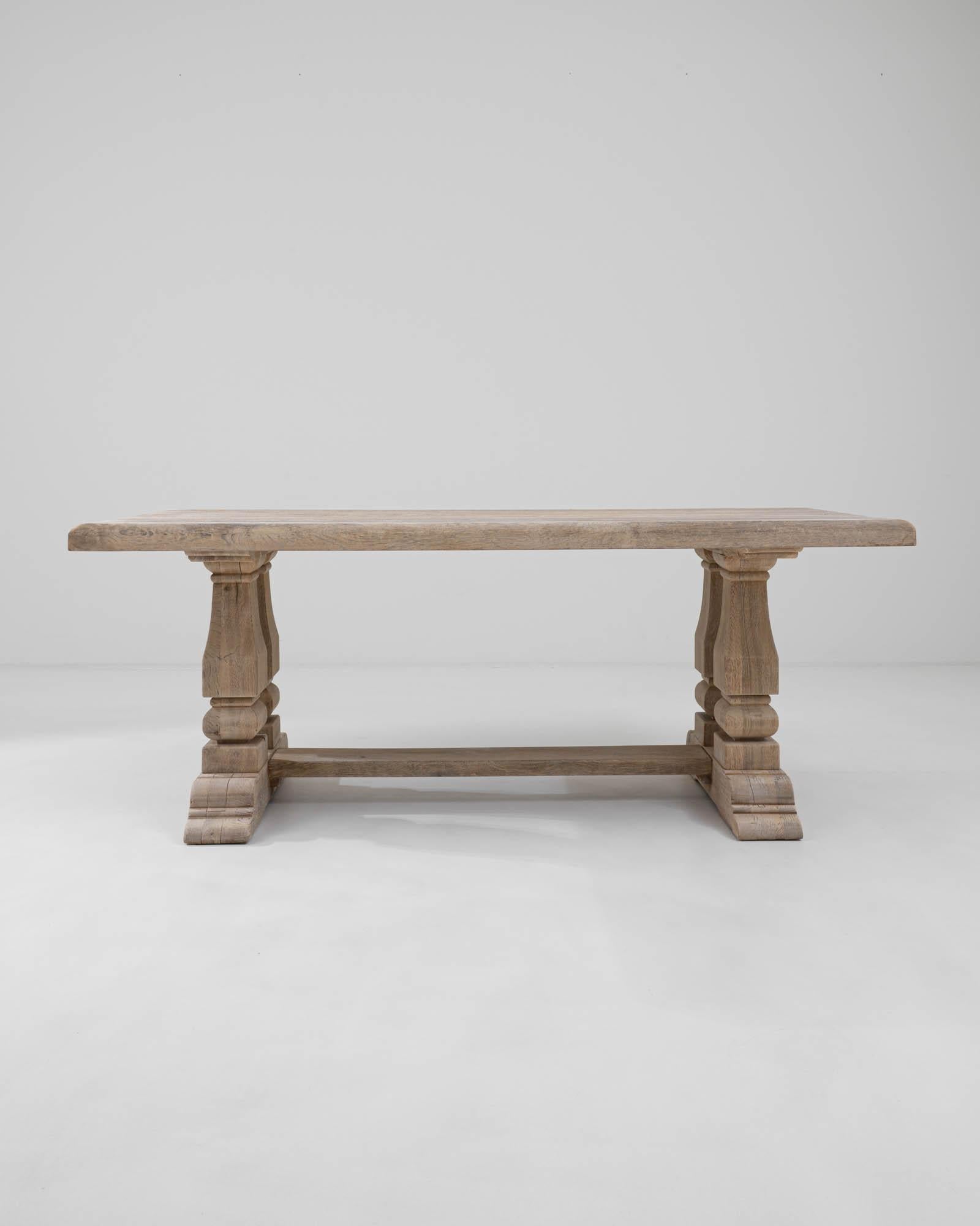A wooden dining table created in 20th century Belgium. This massive dining table exudes both  confident and simultaneously precise and delicate aura. With sumptuously carved legs, carved into a form reminiscent of neo-gothic style, connected into a