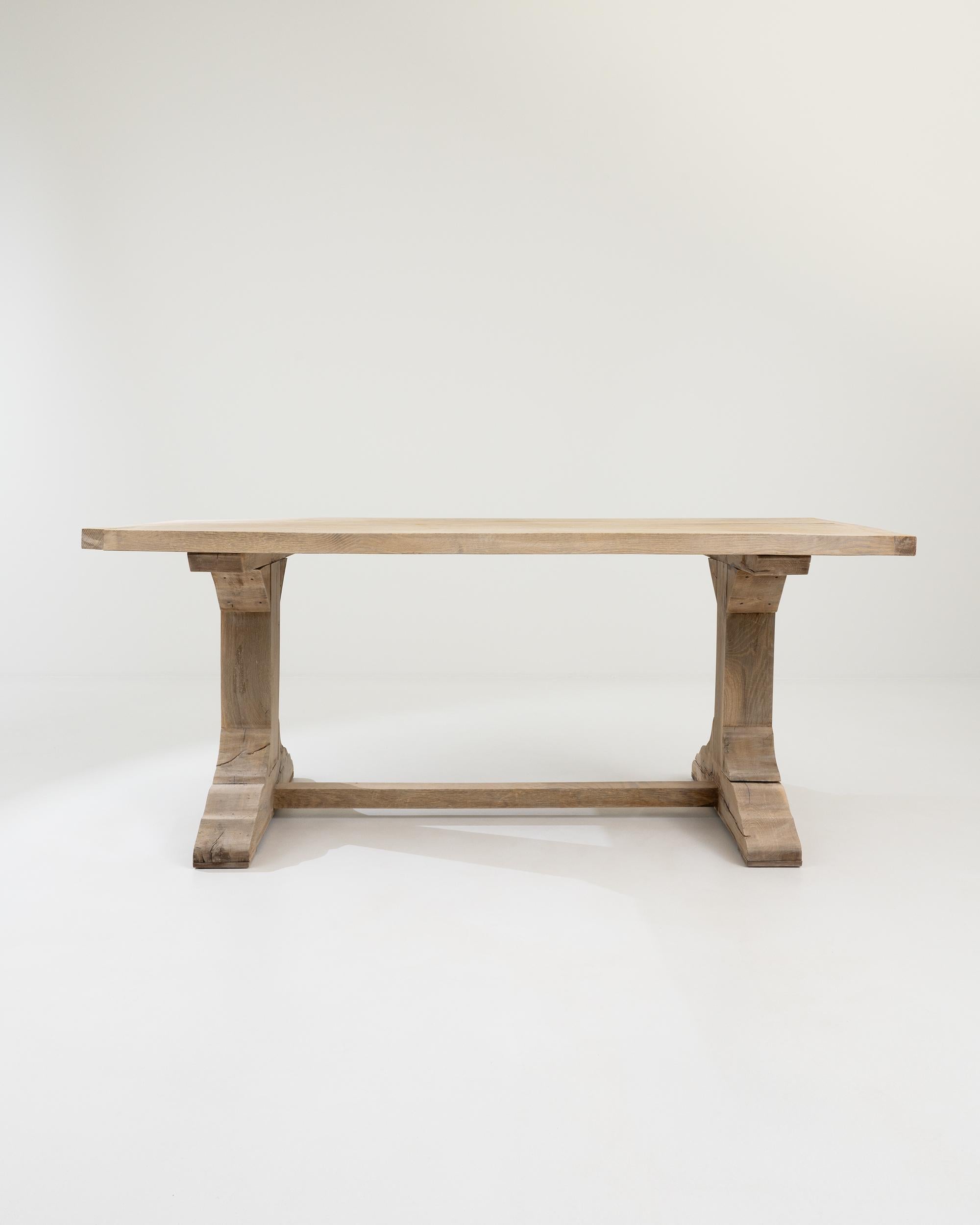 The clean, solid form of this vintage oak dining table has a timeless rustic simplicity. Built in Belgium in the 20th century, a rectangular tabletop rests atop a pair of trestle legs. The subtle contour of the wide feet and the curved form of the