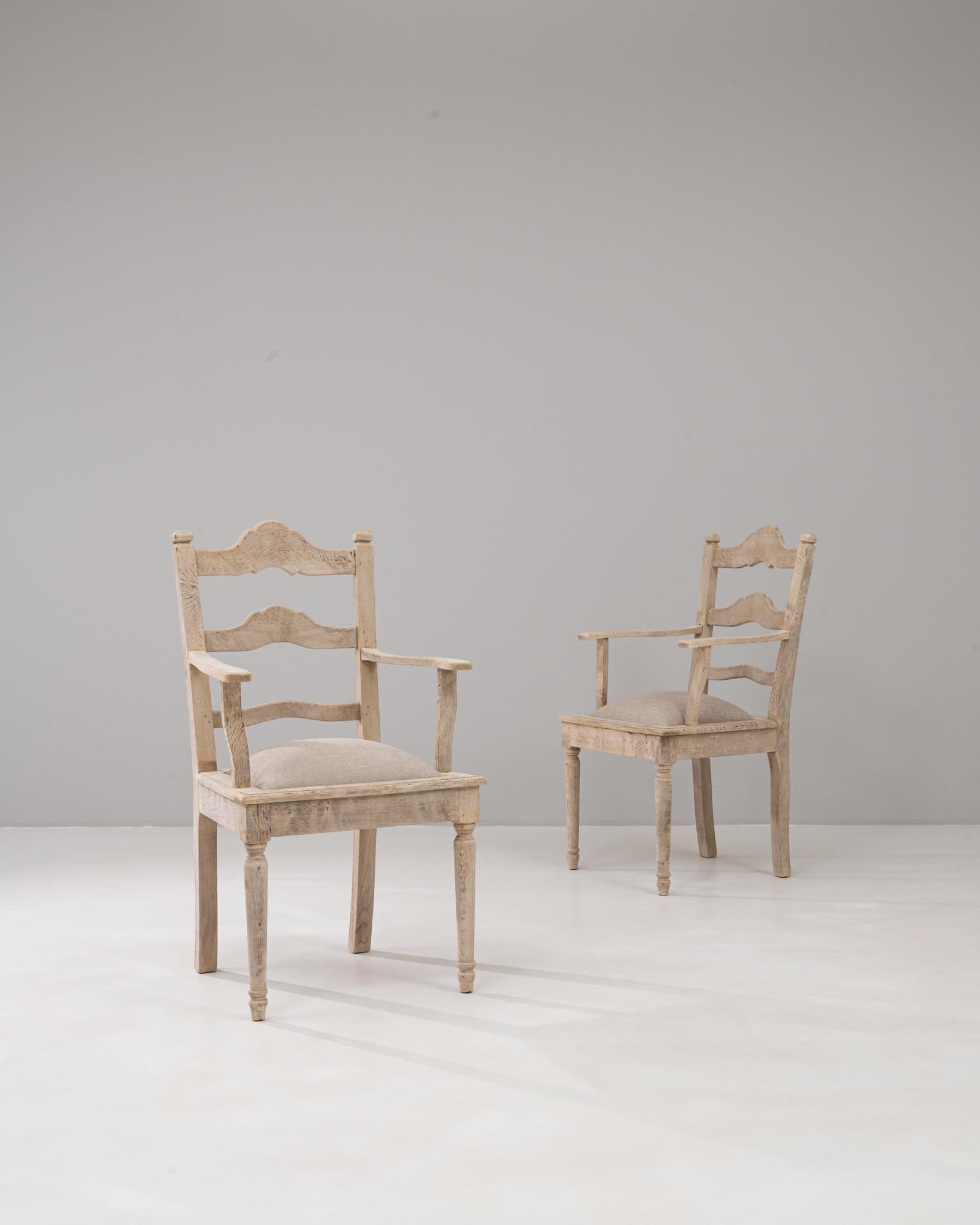 Cette paire de fauteuils belges en chêne du 20e siècle avec sièges rembourrés incarne une élégance rustique enracinée dans l'artisanat européen traditionnel. Les chaises sont dotées d'un cadre en chêne massif avec une finition naturelle légèrement