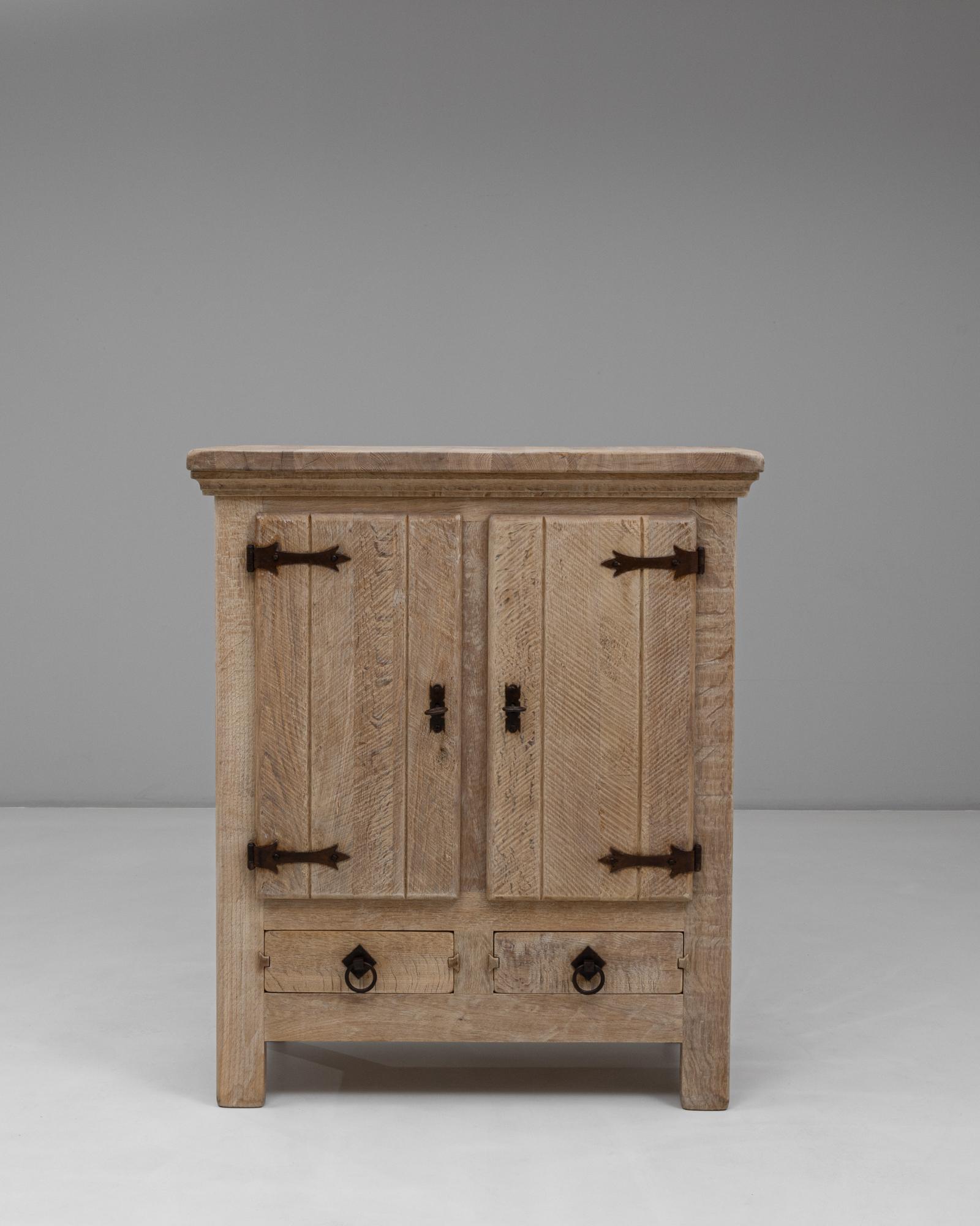 This 20th-century Belgian primitive oak cabinet highlights the beauty of honest craftsmanship and natural materials. Constructed from solid oak with a softly weathered finish, it features double doors with distinctive chevron paneling and