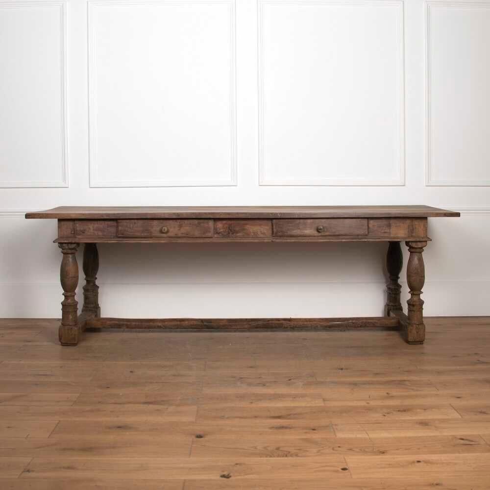 Grande table rustique belge du 20e siècle. 
Cette table substantielle offre deux tiroirs en frise avec un décor profondément sculpté et des poignées en chignon surélevées.
Cette pièce repose sur quatre pieds audacieusement tournés ainsi que sur un