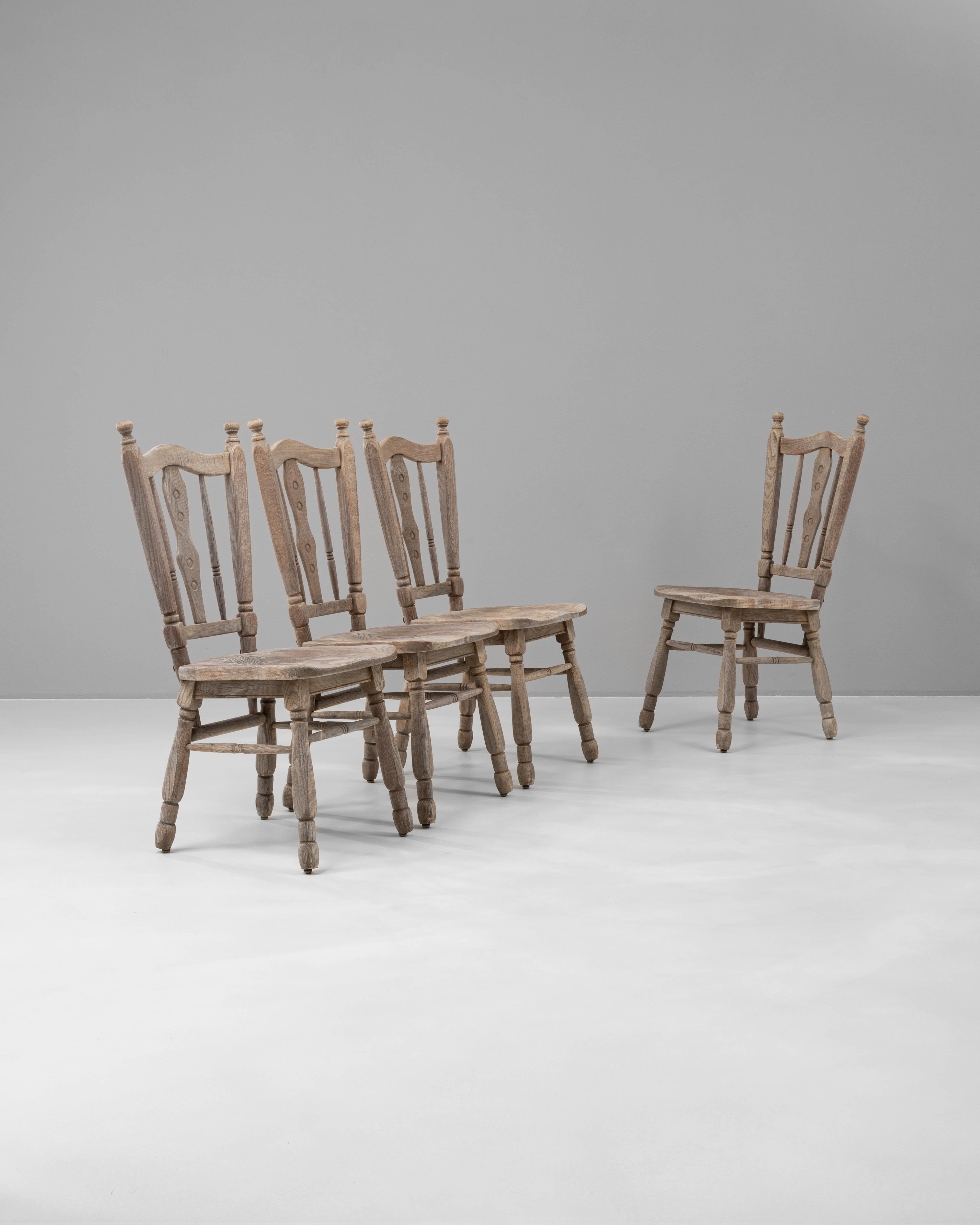 Questo set di quattro sedie da pranzo in quercia belga del XX secolo offre un affascinante fascino rustico, perfetto per dare calore e carattere a qualsiasi spazio da pranzo. Ogni sedia è realizzata in rovere massiccio con una finitura naturale che