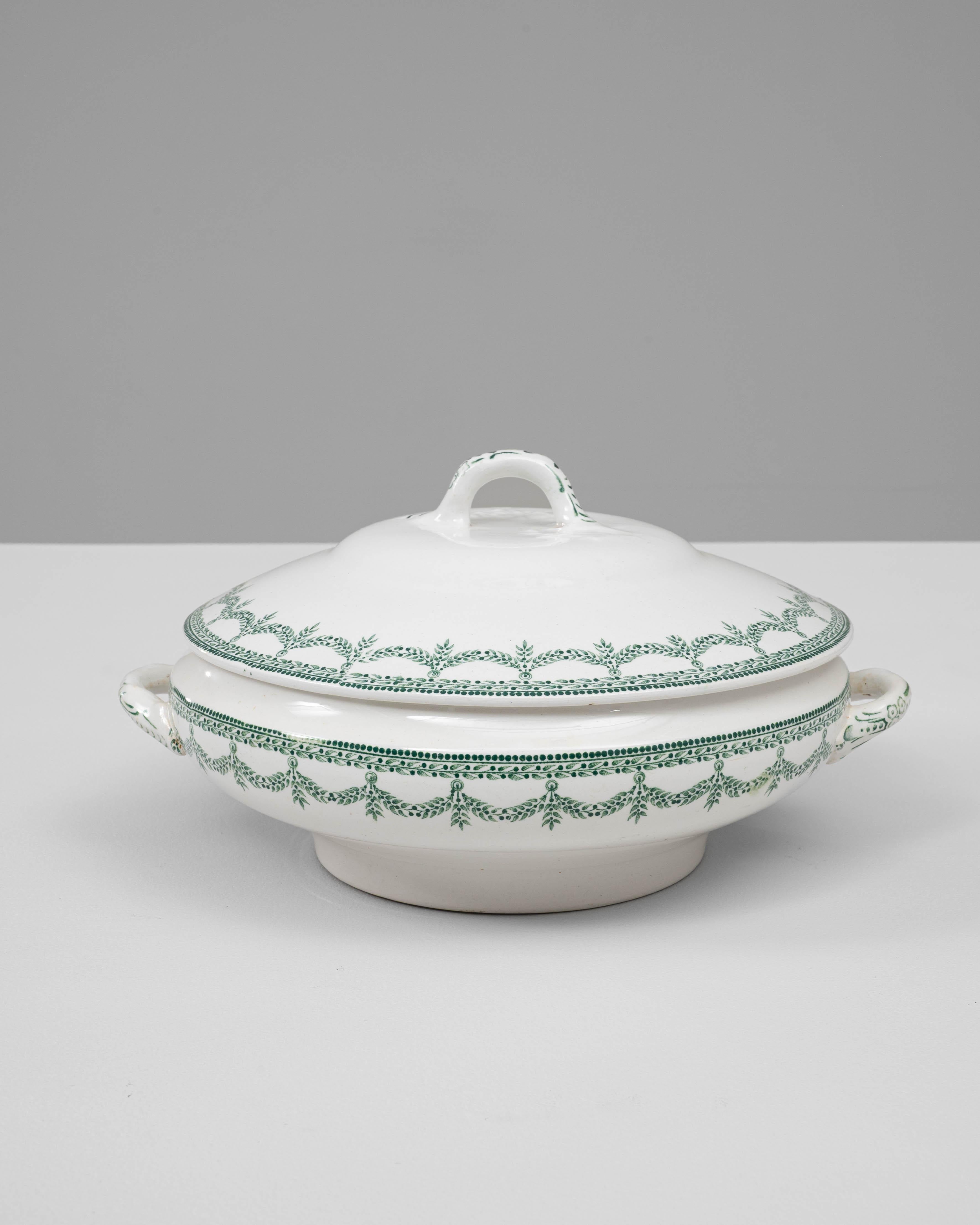 Cette soupière en porcelaine belge du 20e siècle avec couvercle est un exemple magnifiquement préservé de vaisselle européenne raffinée. Fabriqué en porcelaine émaillée blanche, il présente un élégant motif de guirlande verte entourant à la fois le