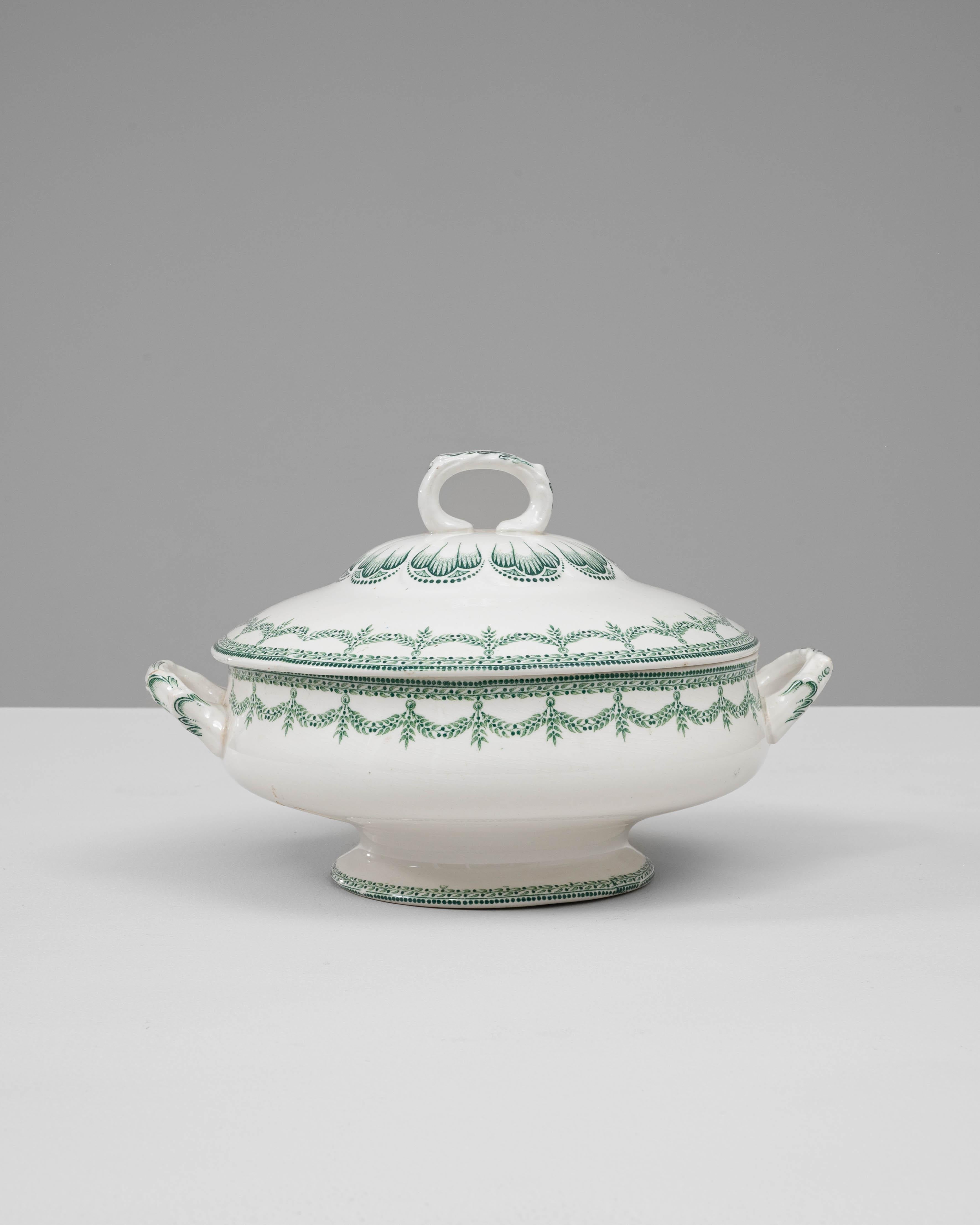 Cette soupière en porcelaine belge du 20e siècle, édition spéciale avec couvercle, présente une exécution élégante et des détails raffinés. Le corps en porcelaine blanche est délicatement orné d'un motif complexe de guirlande verte et d'un fin