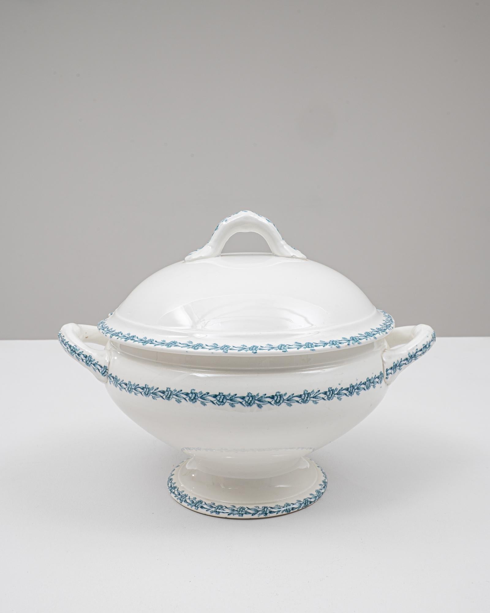 Cette soupière en porcelaine belge du 20e siècle, édition spéciale, présente une silhouette gracieuse sur pied, rehaussée d'une glaçure blanche éclatante et d'une bordure florale bleue finement détaillée. Le couvercle bombé présente une poignée en