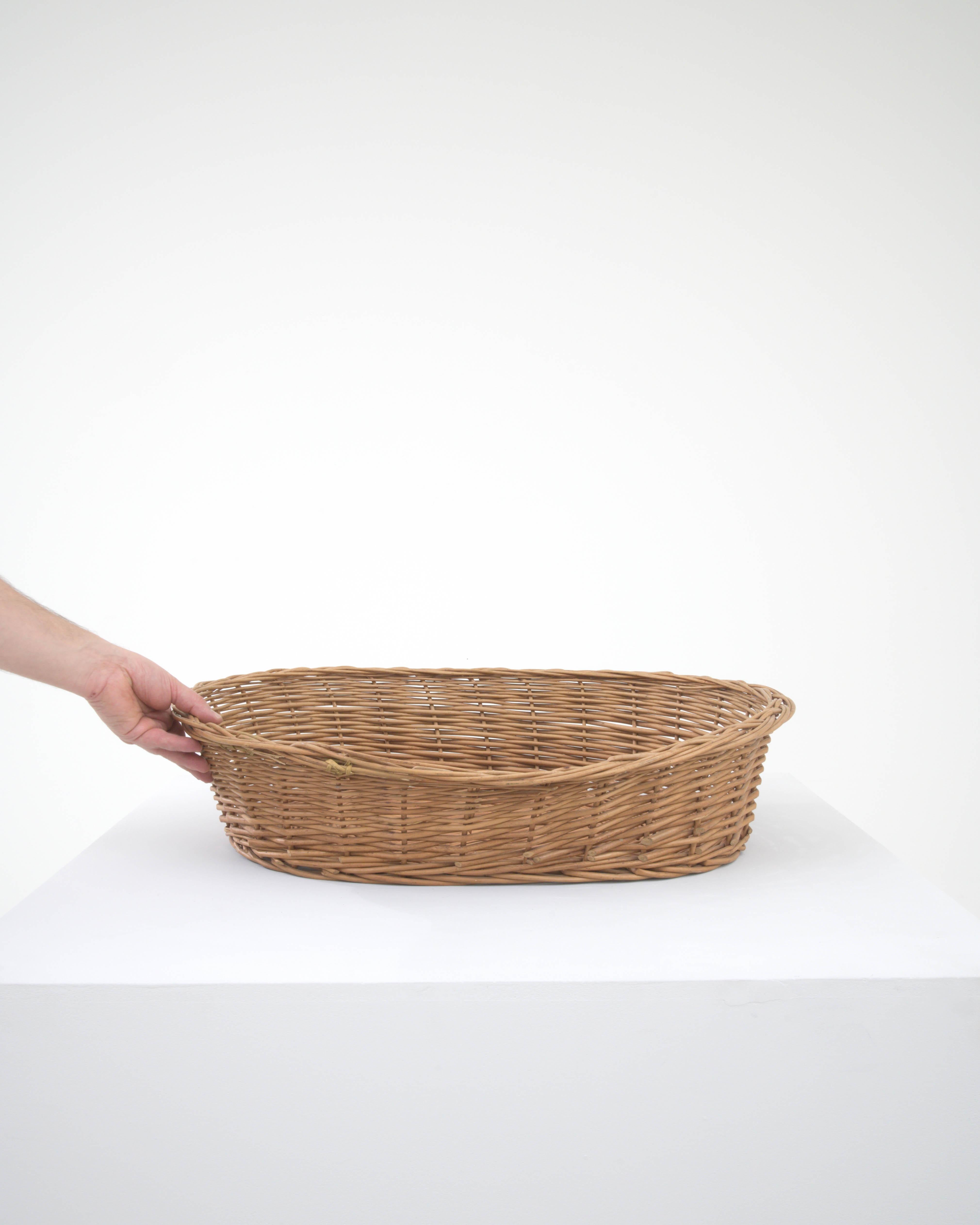 This 20th Century Belgian Wicker Basket brings the allure of rustic craftsmanship into your living space. Its expansive, shallow design makes it an ideal choice for displaying fresh fruit on a kitchen island or serving bread at a family gathering.