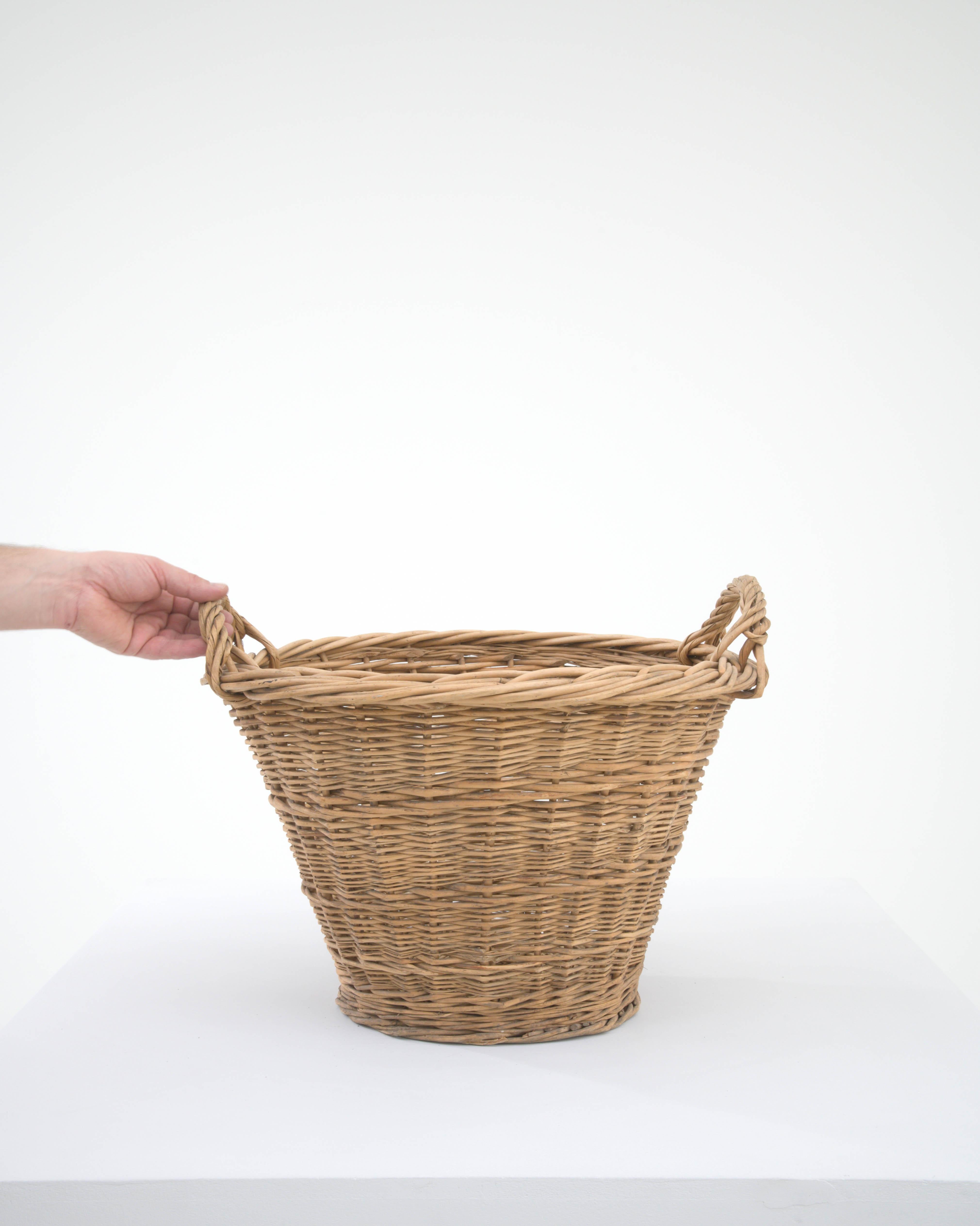 This 20th Century Belgian Wicker Basket is an embodiment of practical beauty, weaving together functionality with the charm of rustic aesthetics. Its robust and curvaceous form offers ample space, perfect for an array of uses, from holding your