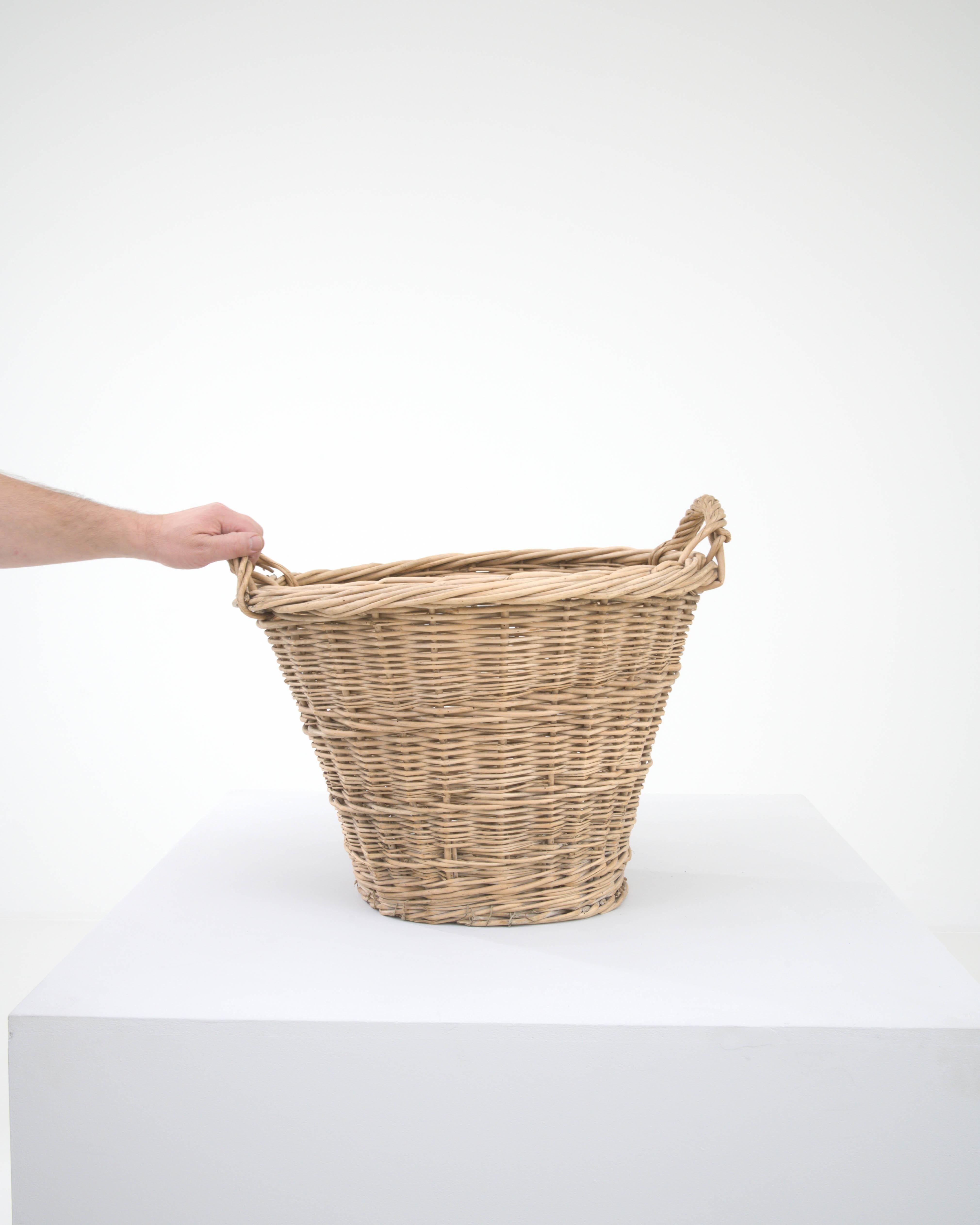 This 20th Century Belgian Wicker Basket is an embodiment of practical beauty, weaving together functionality with the charm of rustic aesthetics. Its robust and curvaceous form offers ample space, perfect for an array of uses, from holding your