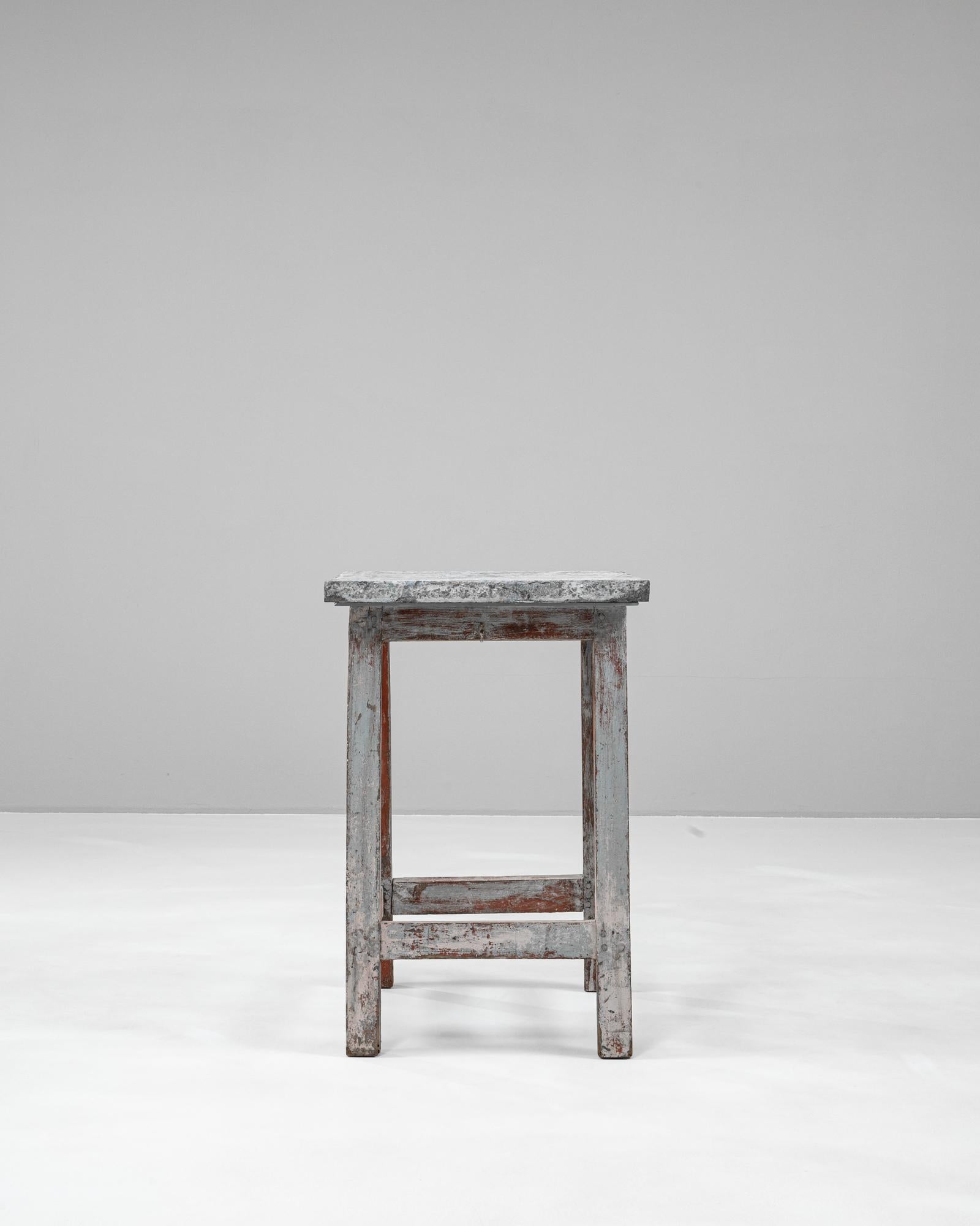 This 20th-century Belgian side table features a rustic, worn wood frame and is topped with an impressive slab of Belgian bluestone. The natural patina on the wood showcases decades of character, with remnants of red and gray paint that add to its