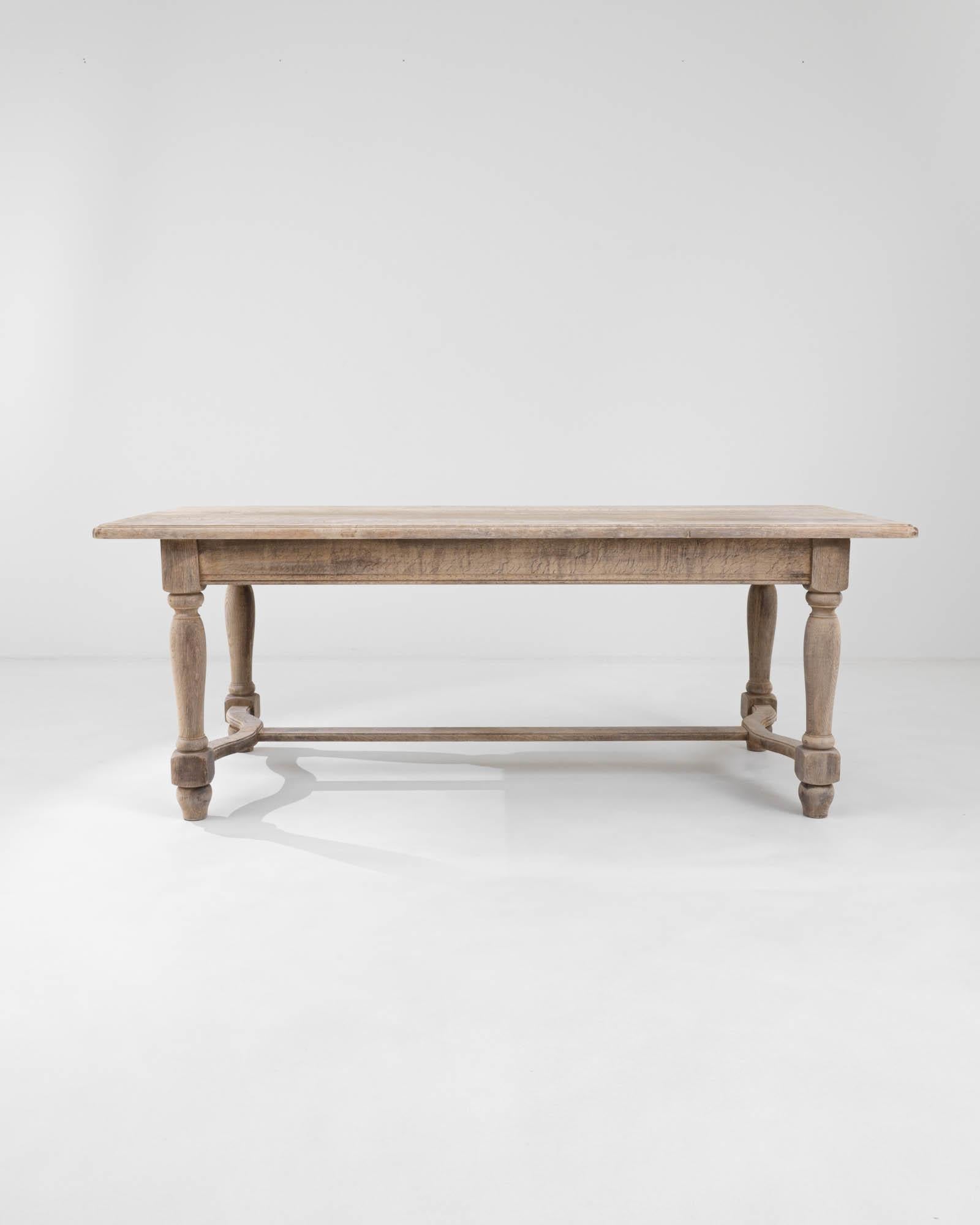 A wooden dining table created in 20th century Belgium. Four gracefully lathed legs descend down from mortise and tenon joints to connect to satisfyingly curved stretchers, creating a classic trestle style dining table. Veins of wood grain run across