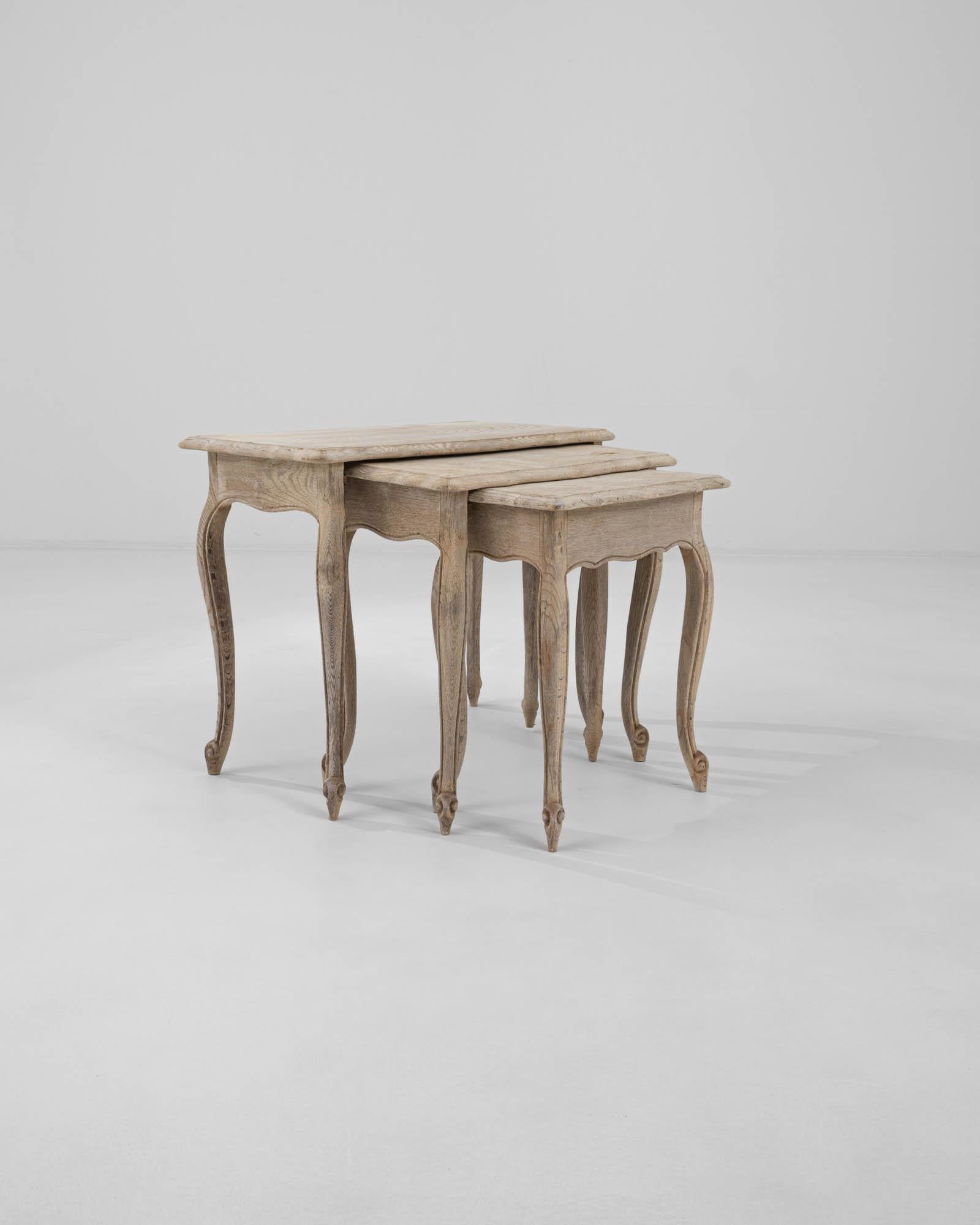 A set of wooden nesting tables created in 20th century Belgium. This set of tables greets one with a cheerful disposition, each of the three tables neatly tucking underneath one another. Elegantly curved aprons and gently tapering legs engender a