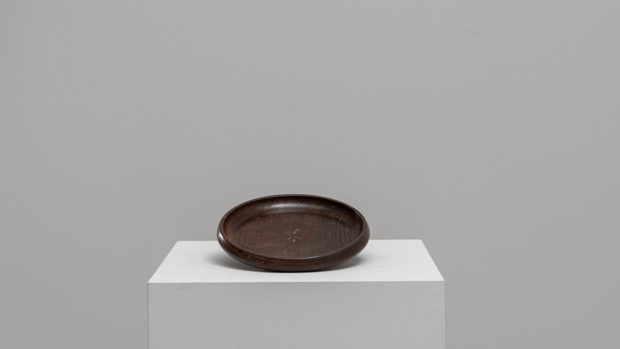This 20th-century Belgian wooden plate embodies simplicity and elegance, making it a versatile addition to your home decor. Crafted from rich, dark wood, this plate features a smooth, rounded design with a subtle lip that enhances its practicality