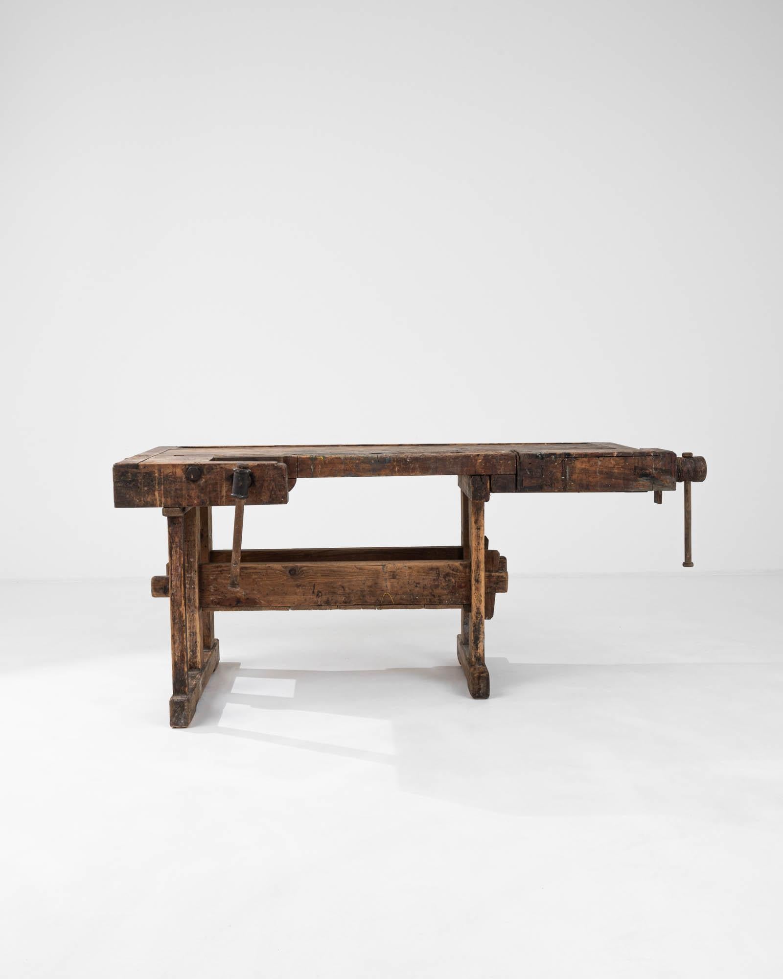 Dieser belgische Holztisch aus dem 20. Jahrhundert ist ein Zeugnis für die dauerhafte Stärke und robuste Schönheit traditioneller Handwerkskunst. Dieser aus Massivholz gefertigte Arbeitstisch strahlt mit seiner abgenutzten Oberfläche und den