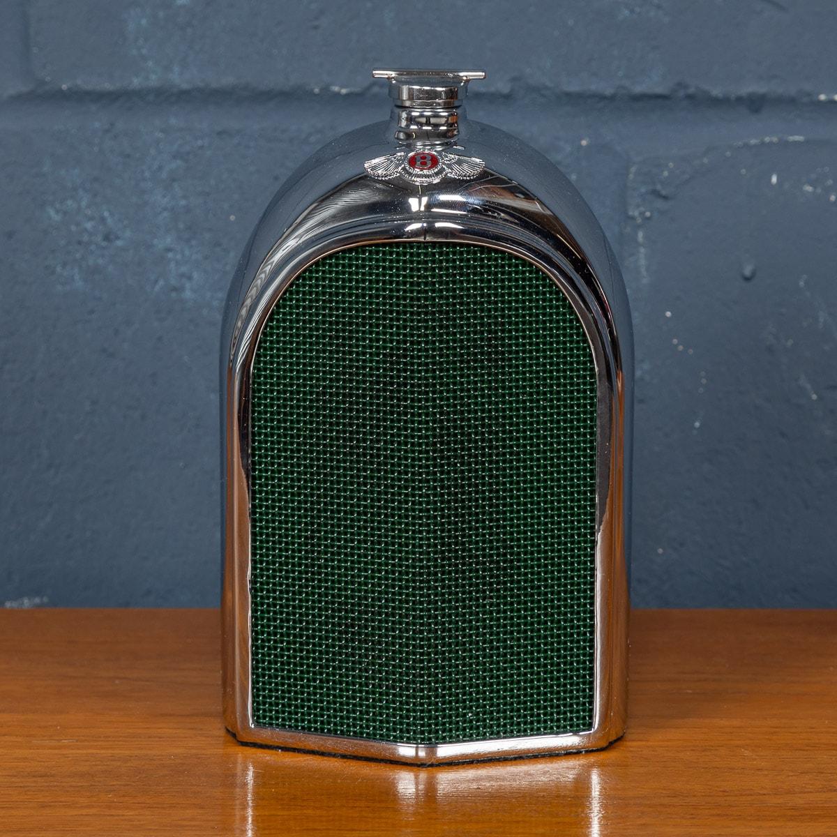 A vintage Bentley chrome radiator grille decanter made in England in the 1960s, bearing the red enamel radiator badge. The decanter is equipped with a “slot” in the casing at the rear allowing visibility of the contents with baize cloth to the base.