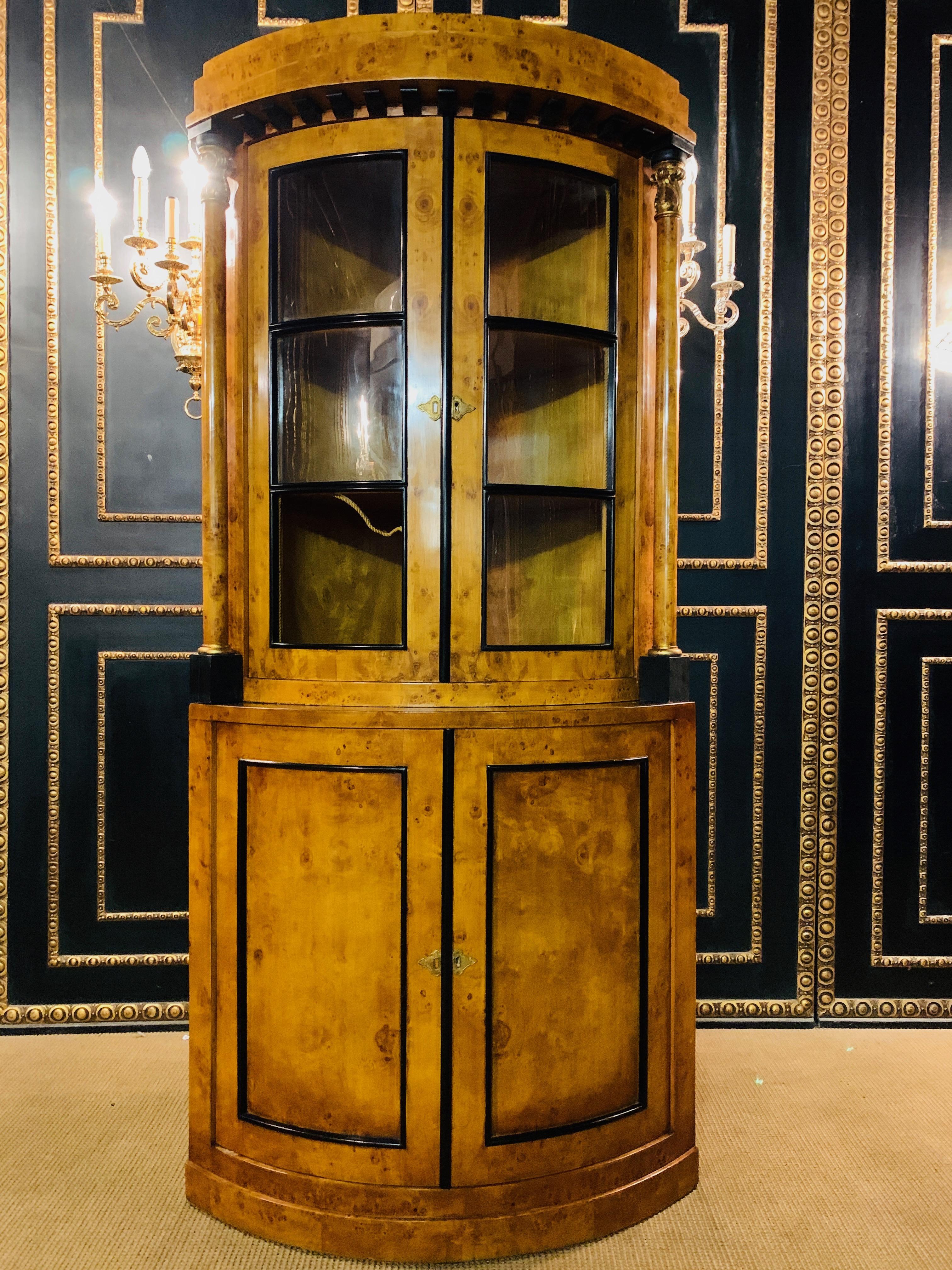 Elegant corner cabinet in Biedermeier style. Bird's eye maple root veneer on solid pine wood. Partly ebonized. Lower body with two doors above a distinctive, overhanging plinth, interior shelves. Narrow over hanging top plate. Above a glazed top