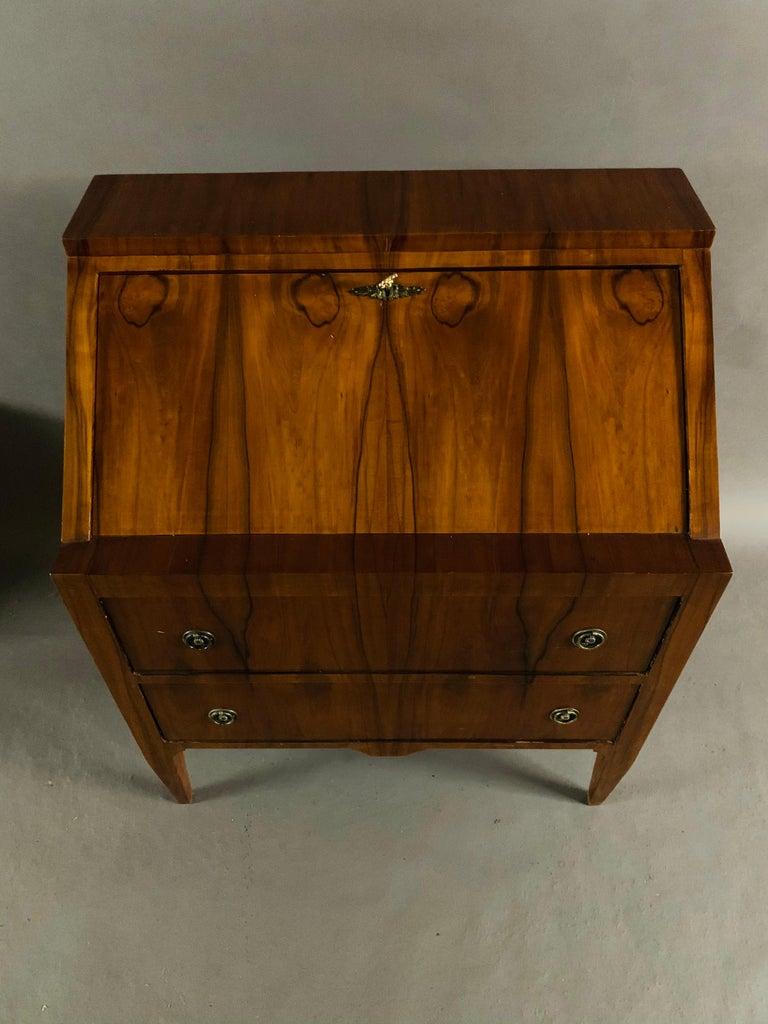 Mahogany on solid softwood. Straight, two-drawer body above short, conical square legs, above an inclined writing flap and staggered office division of drawers and compartments. Classicist fittings with hand rims.
 