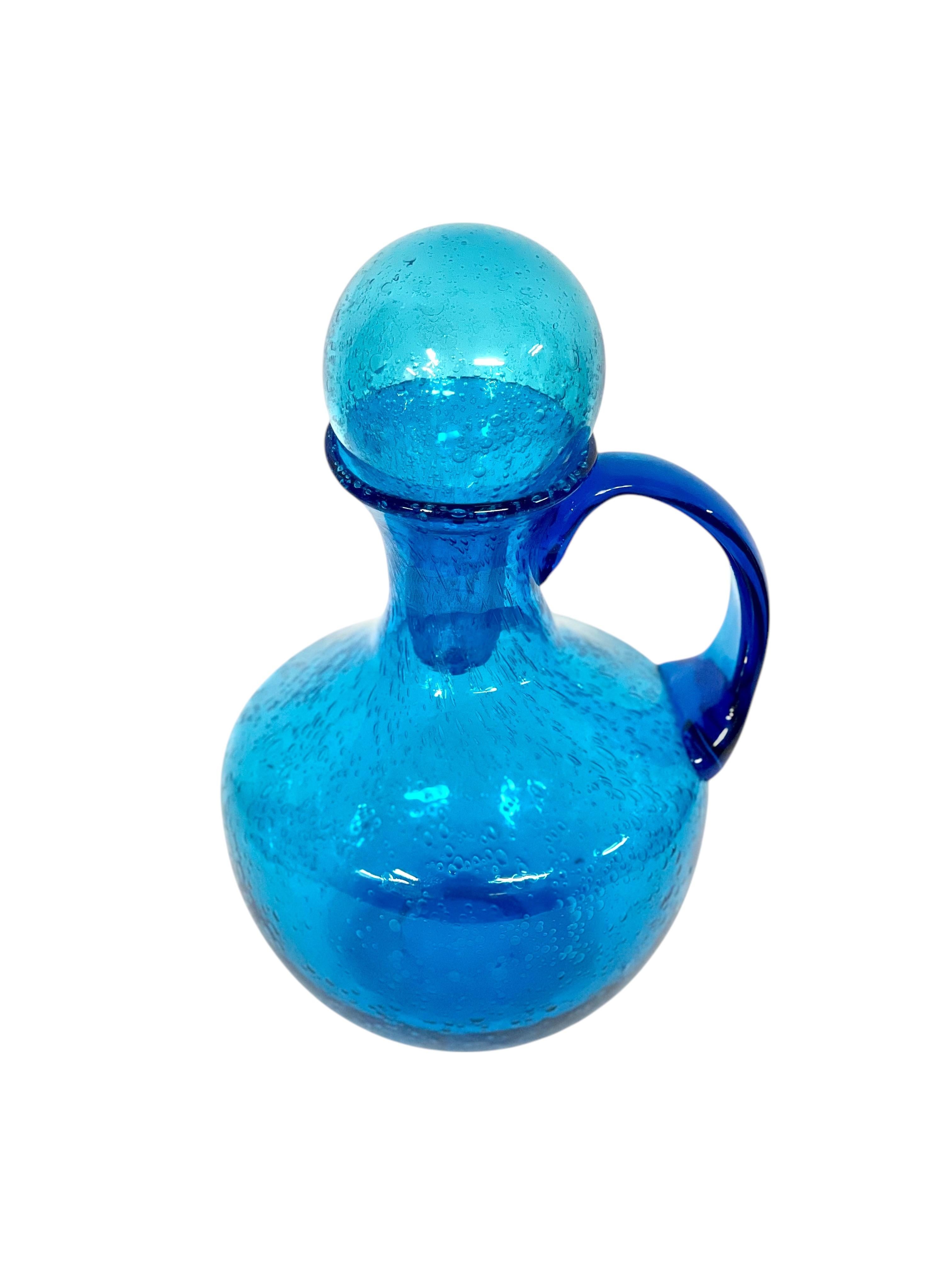 This stunning vintage handblown carafe embodies timeless French craftsmanship, inspired by the style of Biot glassworks. Crafted from vibrant blue bubbled glass, the piece showcases a unique baluster silhouette topped with a spherical stopper,