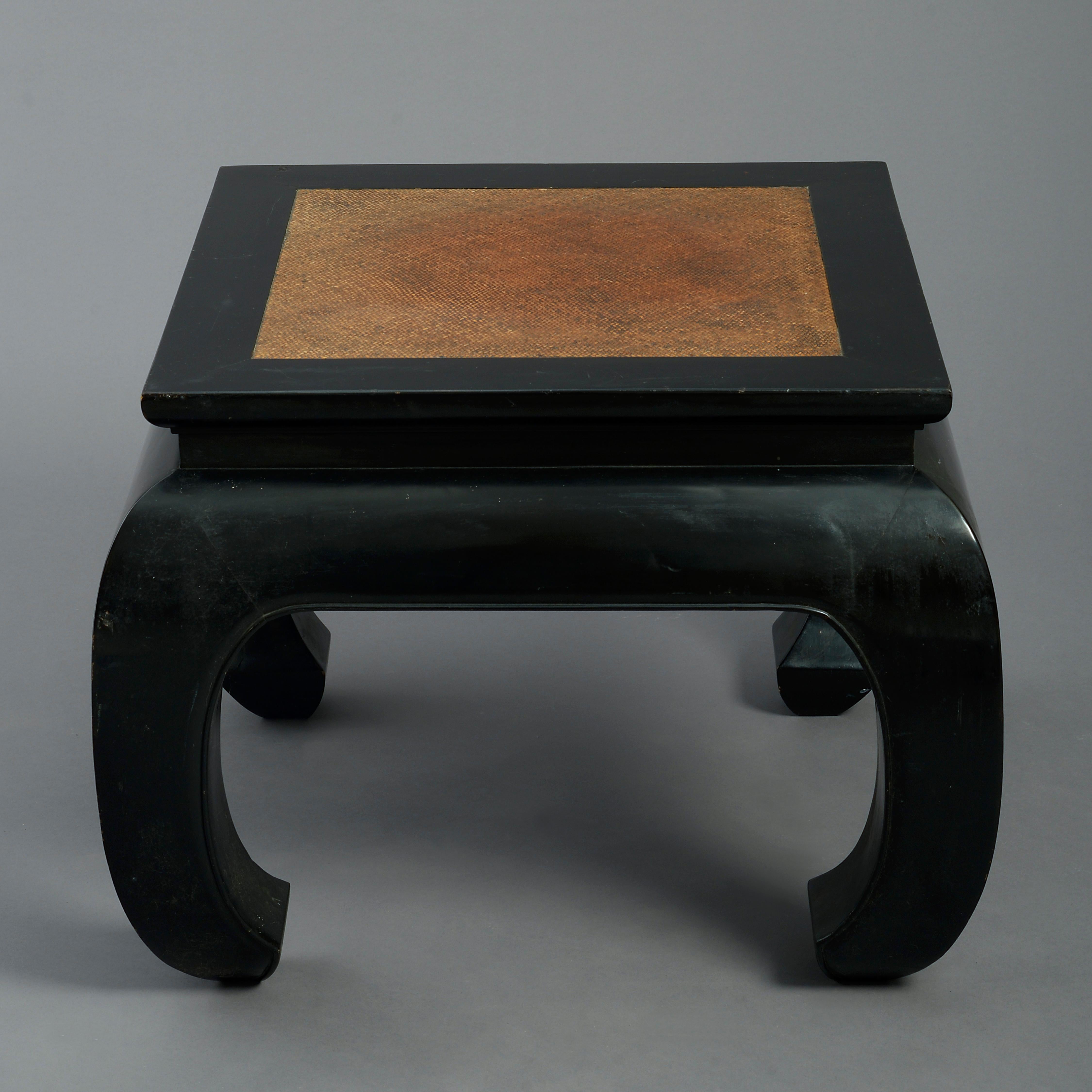 A mid-20th century black lacquer square low table, the top in set with rattan above an apron and shaped feet.