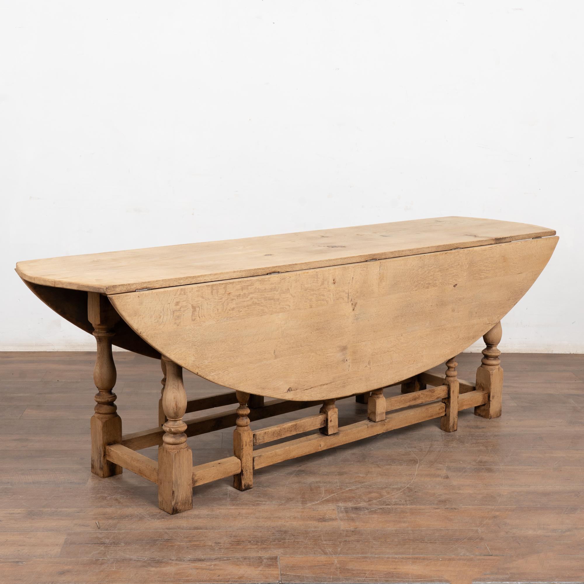 20th-century English wake table crafted in bleached oak with classic dropleaf construction. Gateleg supports allow flexible chair placement when used as a dining table.
With both leaves lowered, the table functions well as a 23