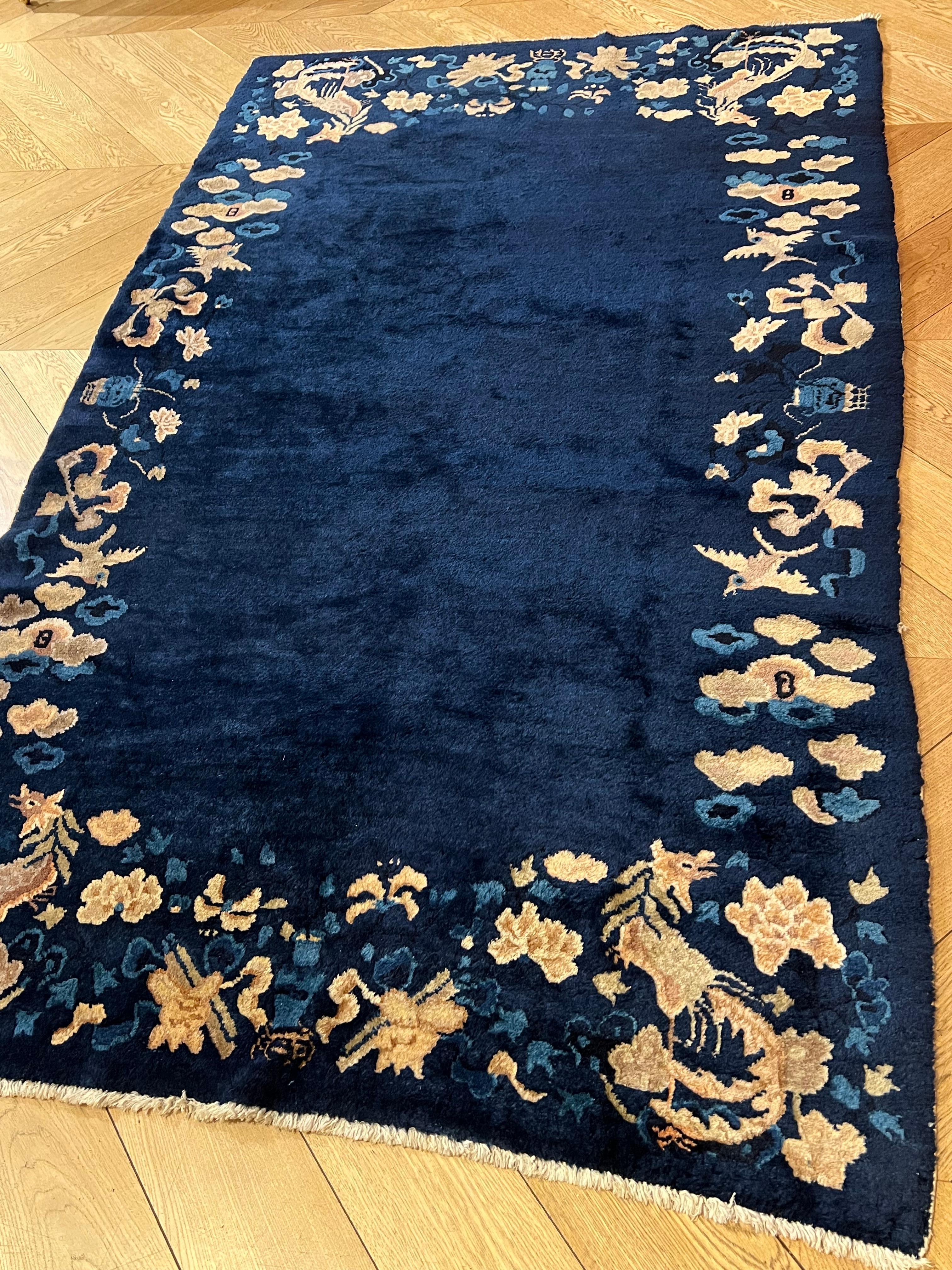 Refined Chinese rug of small size, characterized by a full blue field surrounded by a rich border decorated with flower pots and birds of various shapes. The dominant theme of the decoration is the phoenix placed on the four sides: 
At the