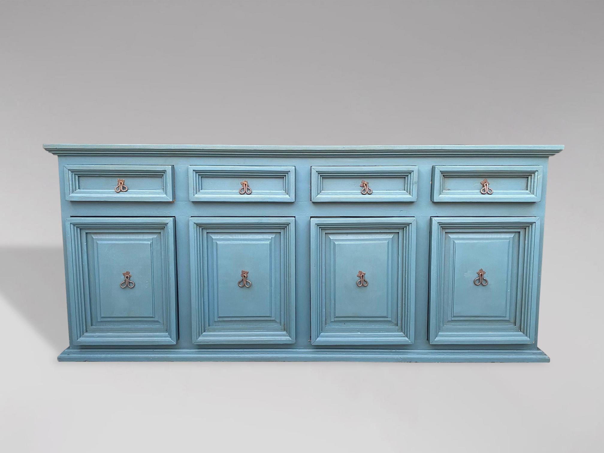 A 20th Century large painted pine dresser base with rectangular moulded top and panelled sides. This charming dresser base or counter offers 4 frieze drawers above 4 cupboard doors with shelves to interior all comprising wrought iron shaped handles,
