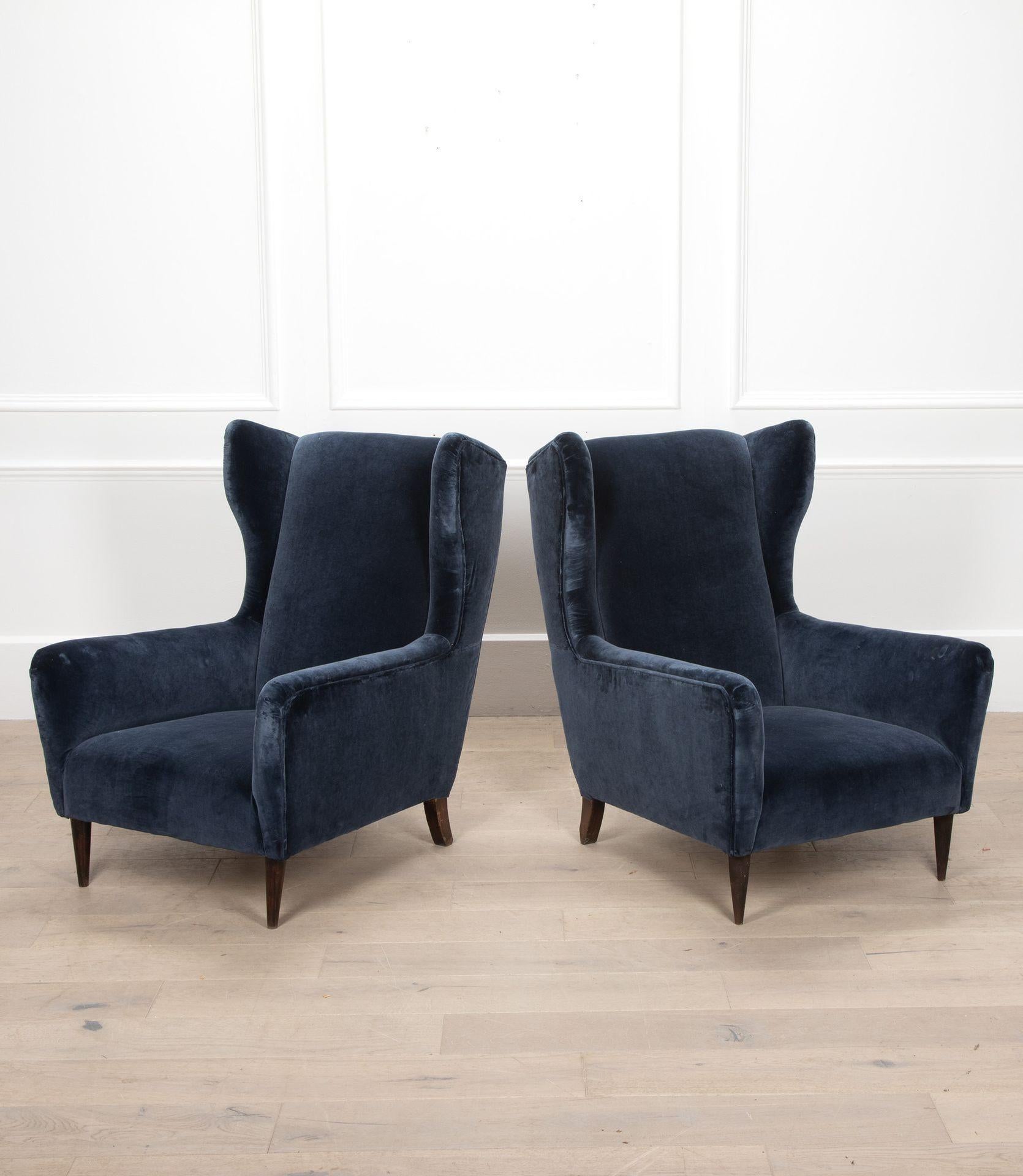 Pair of 20th Century Italian blue velvet high-back armchairs. 
Mid-Century in style with wooden feet.
With some signs of wear and chips to the rear of some feet.