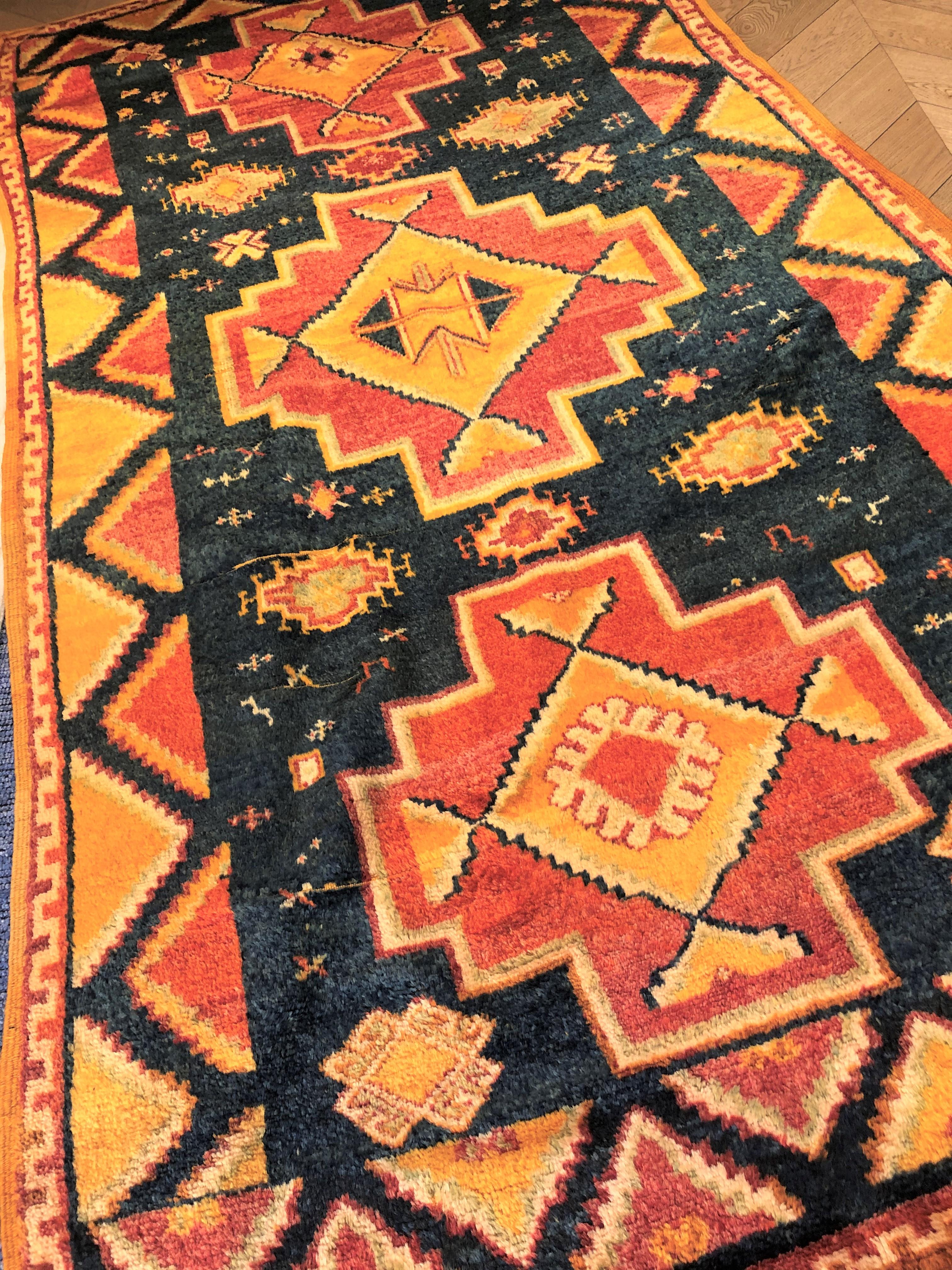 Tapis berbère, fabrication ancienne, qualité oouazouite, caractérisé par un cadre en laine jaune safran. Ces tapis ont une décoration qui dépeint la vie quotidienne de la tribu ainsi que des thèmes classiques de la tradition musulmane. Trois