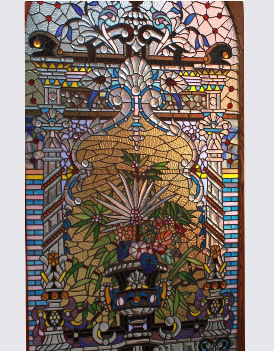 Bogenrief Studios stained glass window panel, 20th century, tall arched rectangular panel composed of numerous shaped and faceted glass inserts forming a central design of an urn issuing exotic flowers, etched signature and numbered