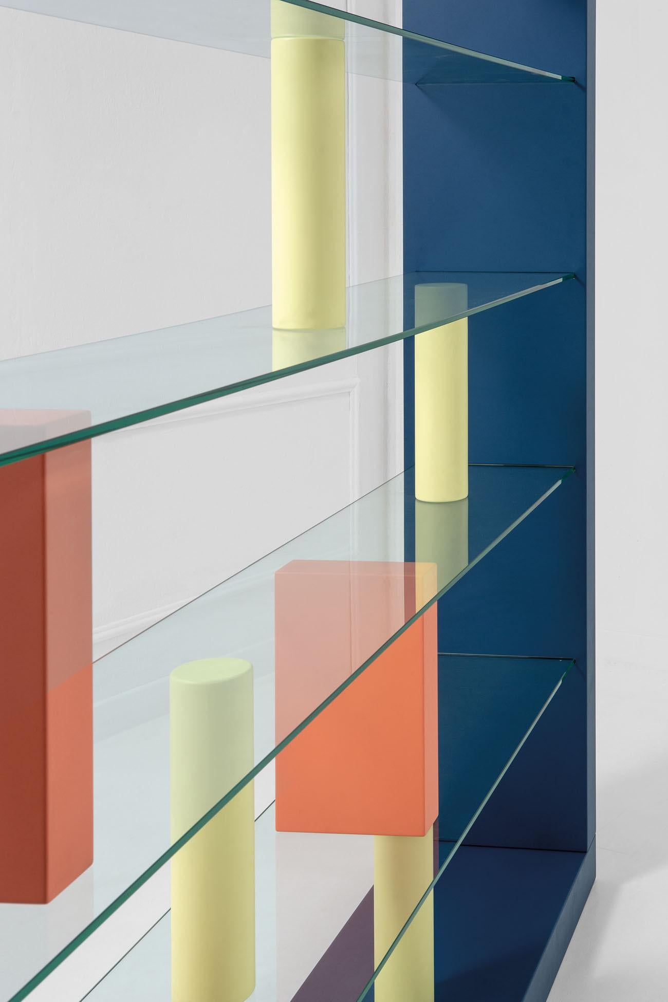 20th-century bookcase Giorno by Ettore Sottsass consisting of a rectangular structure in lacquered blue wood, crystal shelves, and lacquered orange and yellow wood supporting blocks in geometrical shapes.
Production Shopenauer (Fontana Arte),