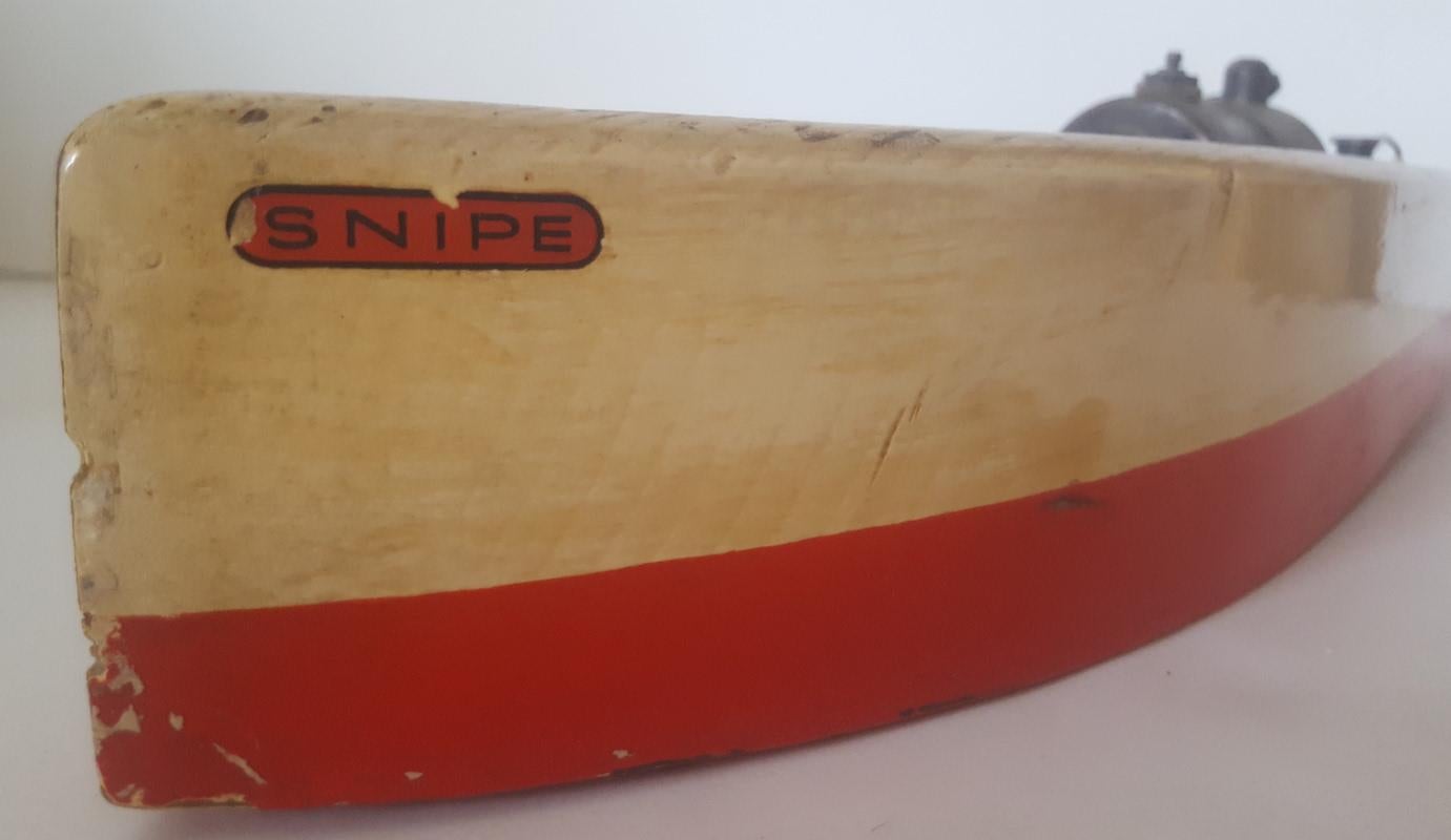 A toy or model wooden boat, powered by a miniature steam engine. Made and sold in England circa 1930- 1935, this painted wood hull with natural wood sealed decks is original, but not in clean or working order. It has been well used and sailed (back