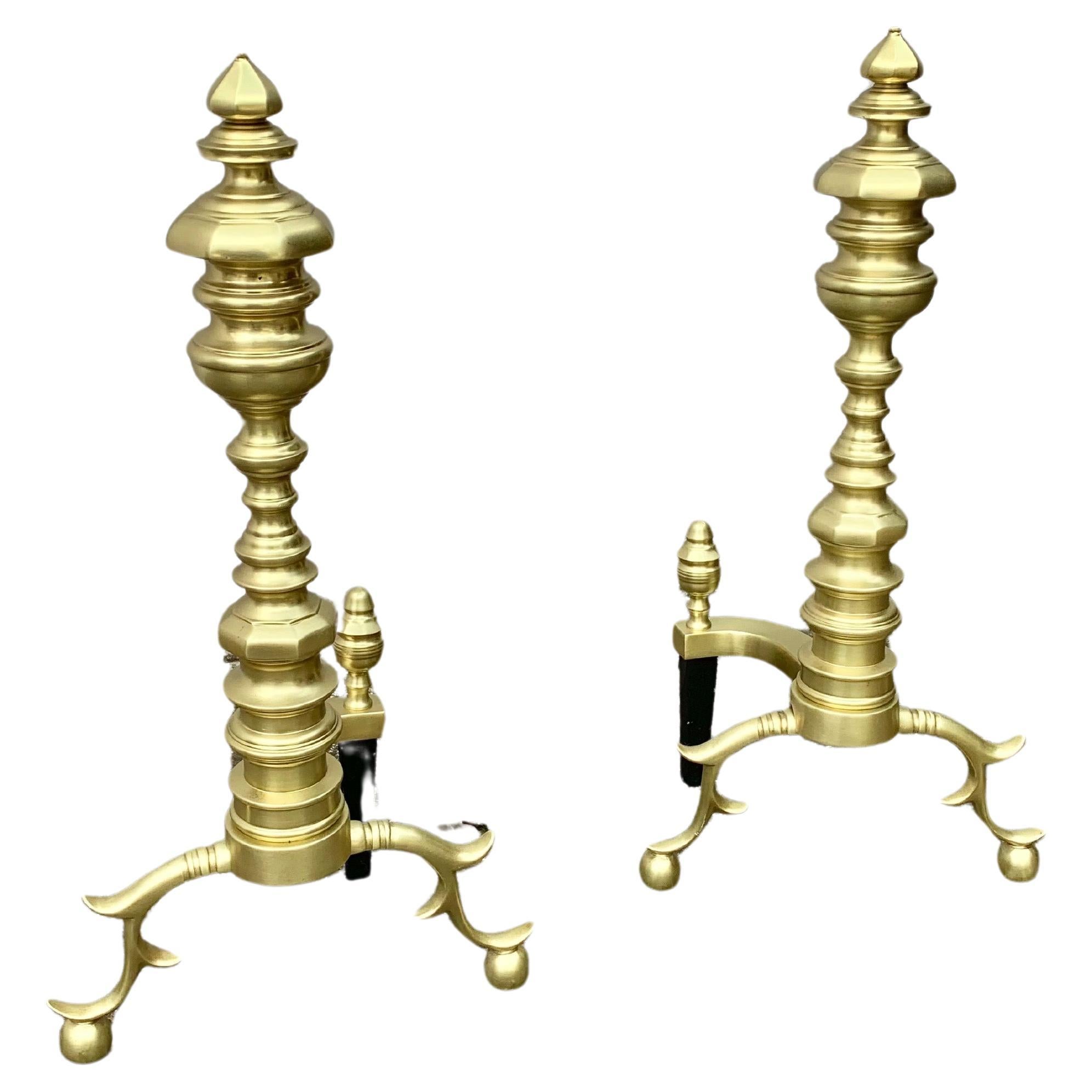 This pair of 20th Century Beehive Style Andirons were crafted from brass and iron in the 1900's. Both pieces feature turned finial capitals on sectional columns rising from spurred cabriole legs and ball feet. The curved back arms present finial