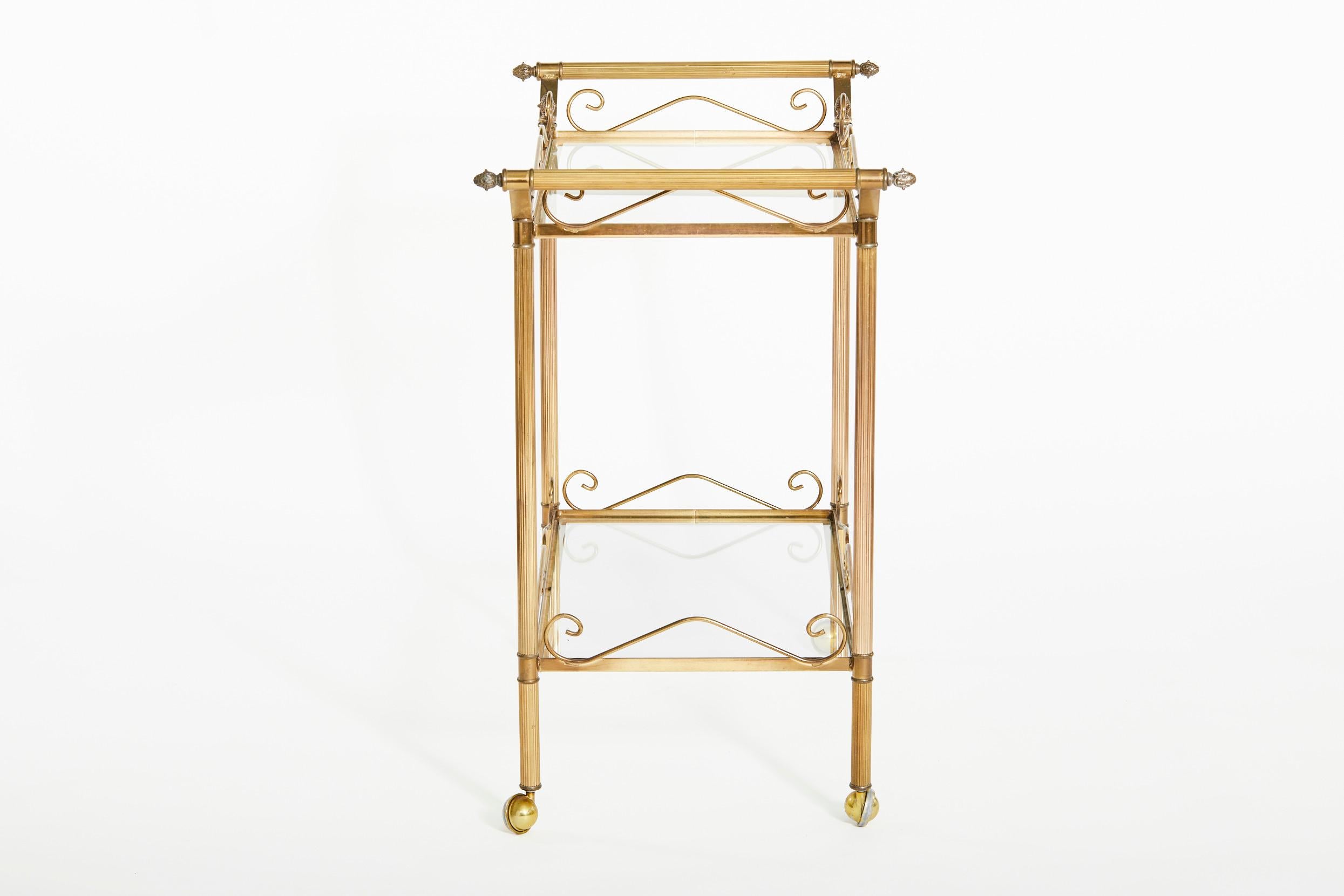 Beautiful mid 20th century brass frame with glass design details two tiered wheeled bar cart. The bar cart features top and lower glass shelve, two side handle with exterior design details. The cart is in great condition. Minor wear consistent with