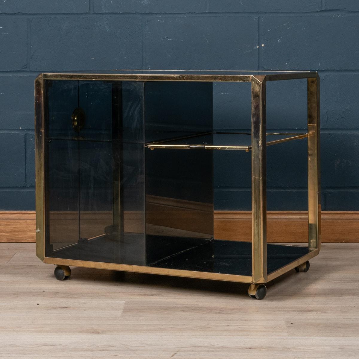 An elegant brass framed cocktail trolley designed by Willy Rizzo for Mario Sabot, produced in Italy in the 1970s. The dark smoked glass panels are framed by a brass structure on castors, one half with open shelves with a pull-out tray, the other