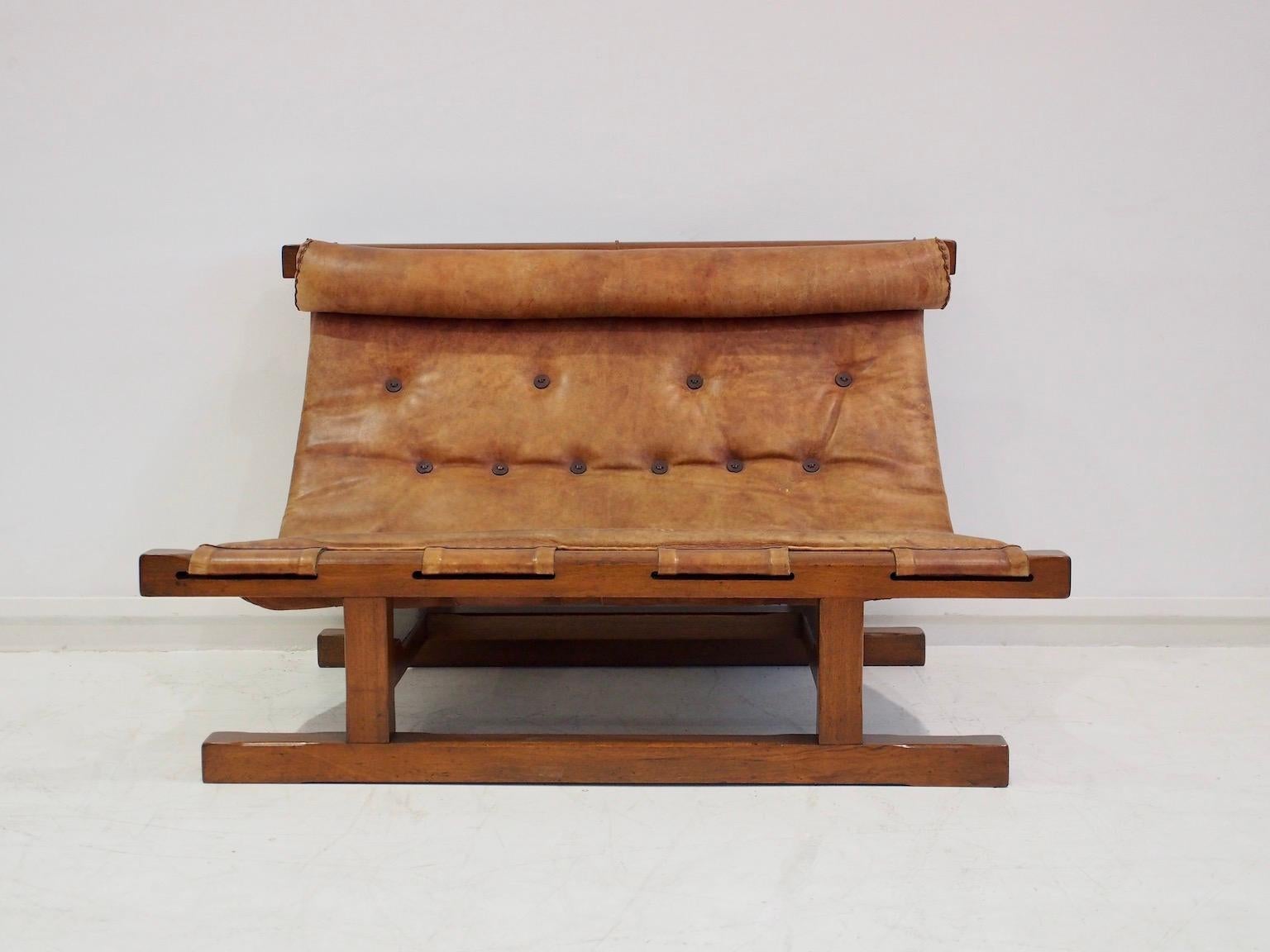 Small sofa or loveseat made in Brazil in the 1960s. Brown leather seat and back decorated with furniture nails and is attached to a solid wood frame with leather straps. Some patina and marks. Pair of lounge chairs in set sold separately.