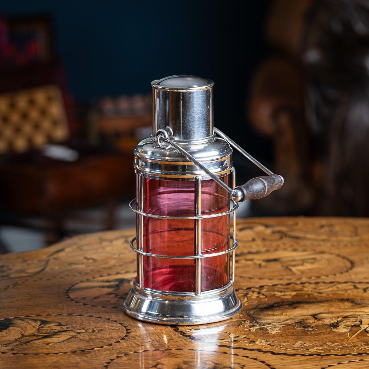 20th Century British silver-plated cocktail shaker designed as a ship lantern, hand crafted by Asprey & Co. It features a red glass centre encased in a silver-plated lantern-shaped body. The shaker includes a removable cork plug with a built-in