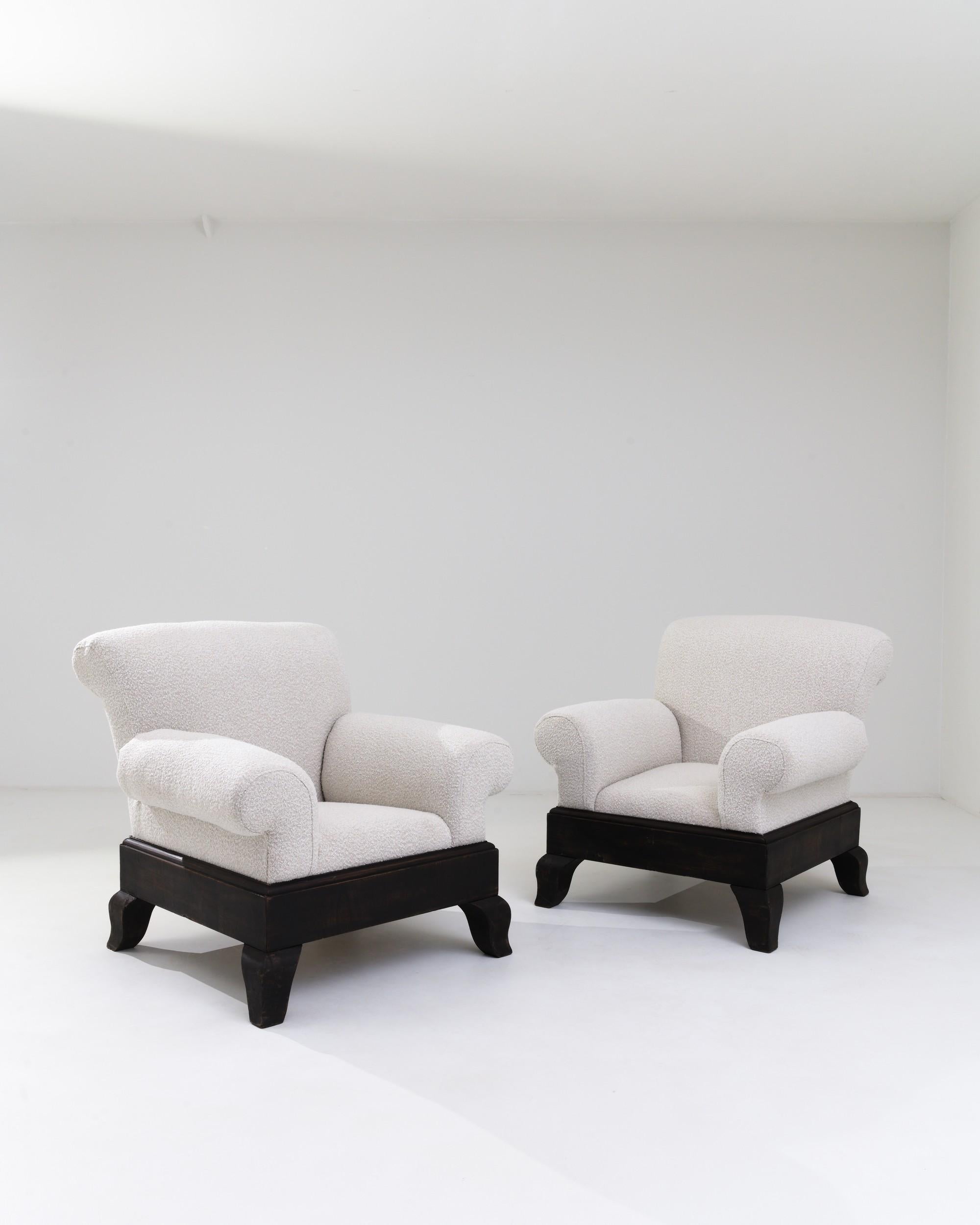 A pair of wooden upholstered armchairs created in 20th century United Kingdom. With a wide base and gracefully splayed arms, these chairs offer a sturdy and comfortable resting place. A fresh off-white boucle upholstery has been added to the