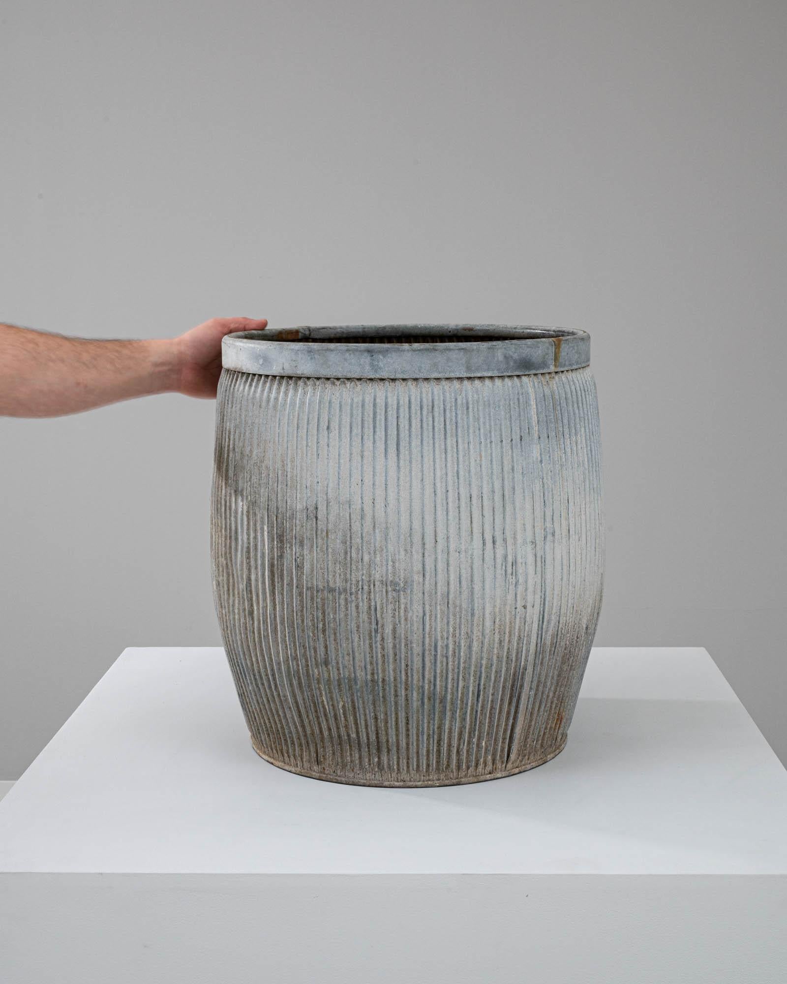 This 20th-century British zinc planter is a striking addition to any space that values a blend of industrial charm and pastoral beauty. Its cylindrical shape is accentuated by vertical ridges that add texture and visual interest, while the zinc