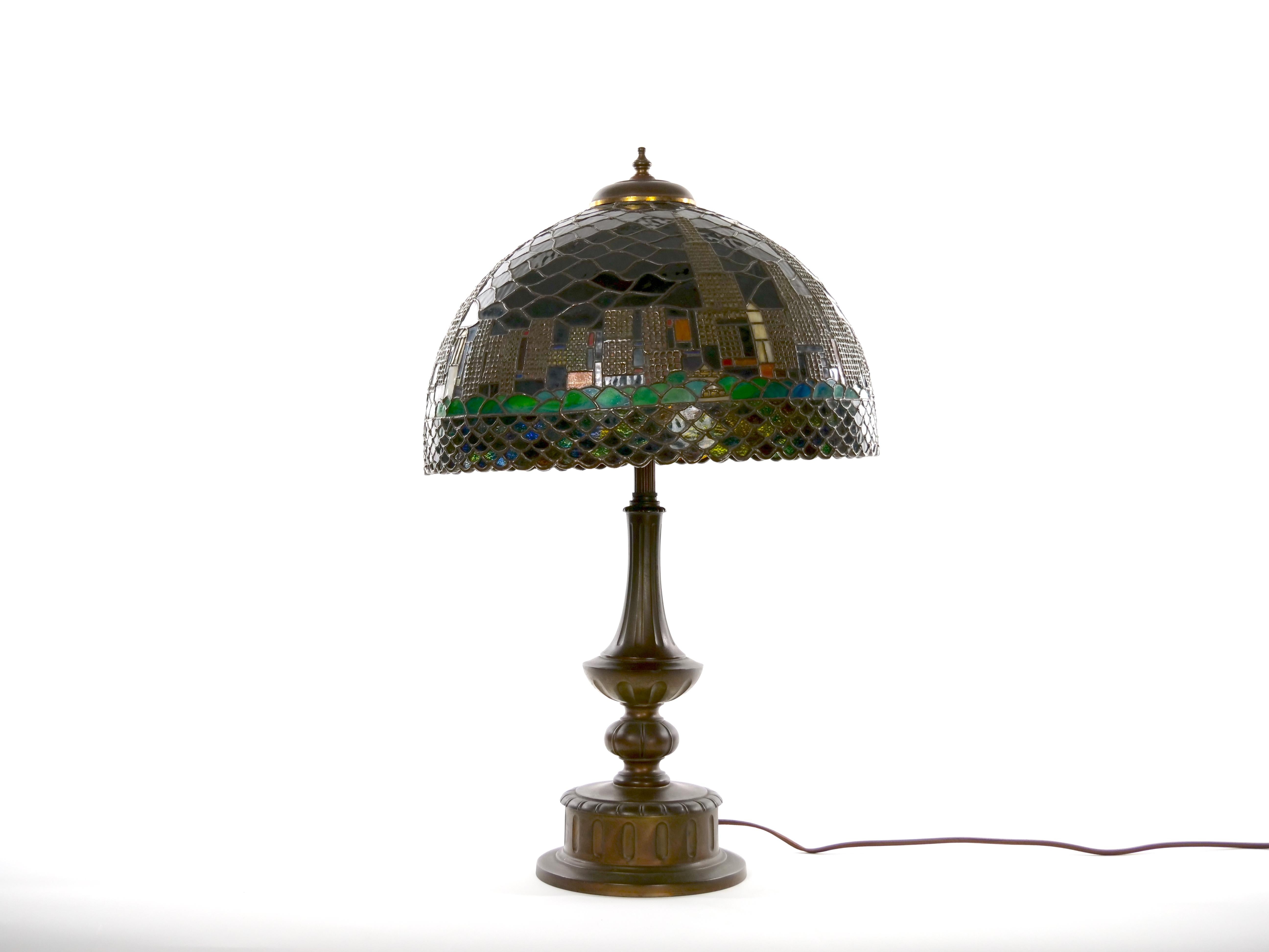 Late 20th century bronze with leaded glass shade table lamp. The lamp features a leaded shade depicting the Chicago skyline resting on a round bronze metal base with  three sockets. The shade signed Frank Kucera. It measures 25 inches high X 15